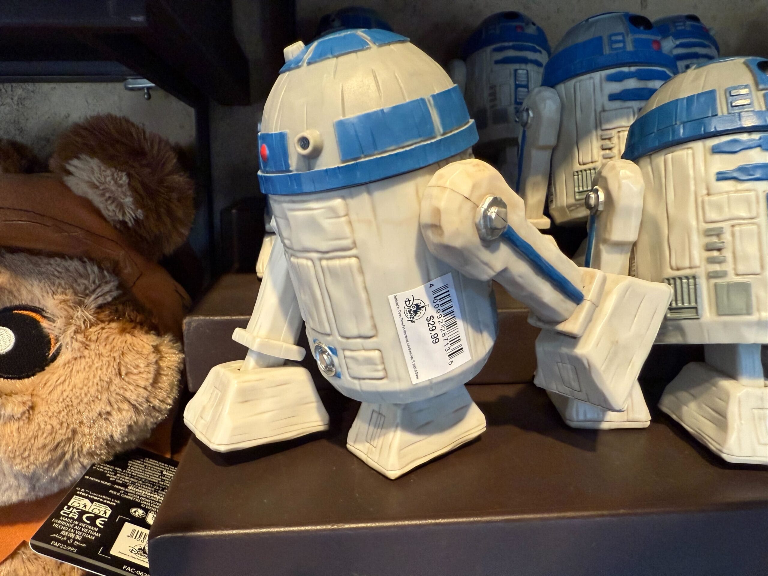 A ceramic R2-D2 figurine with a barcode sticker, displayed alongside other R2-D2 figures, evokes Disneyland magic.