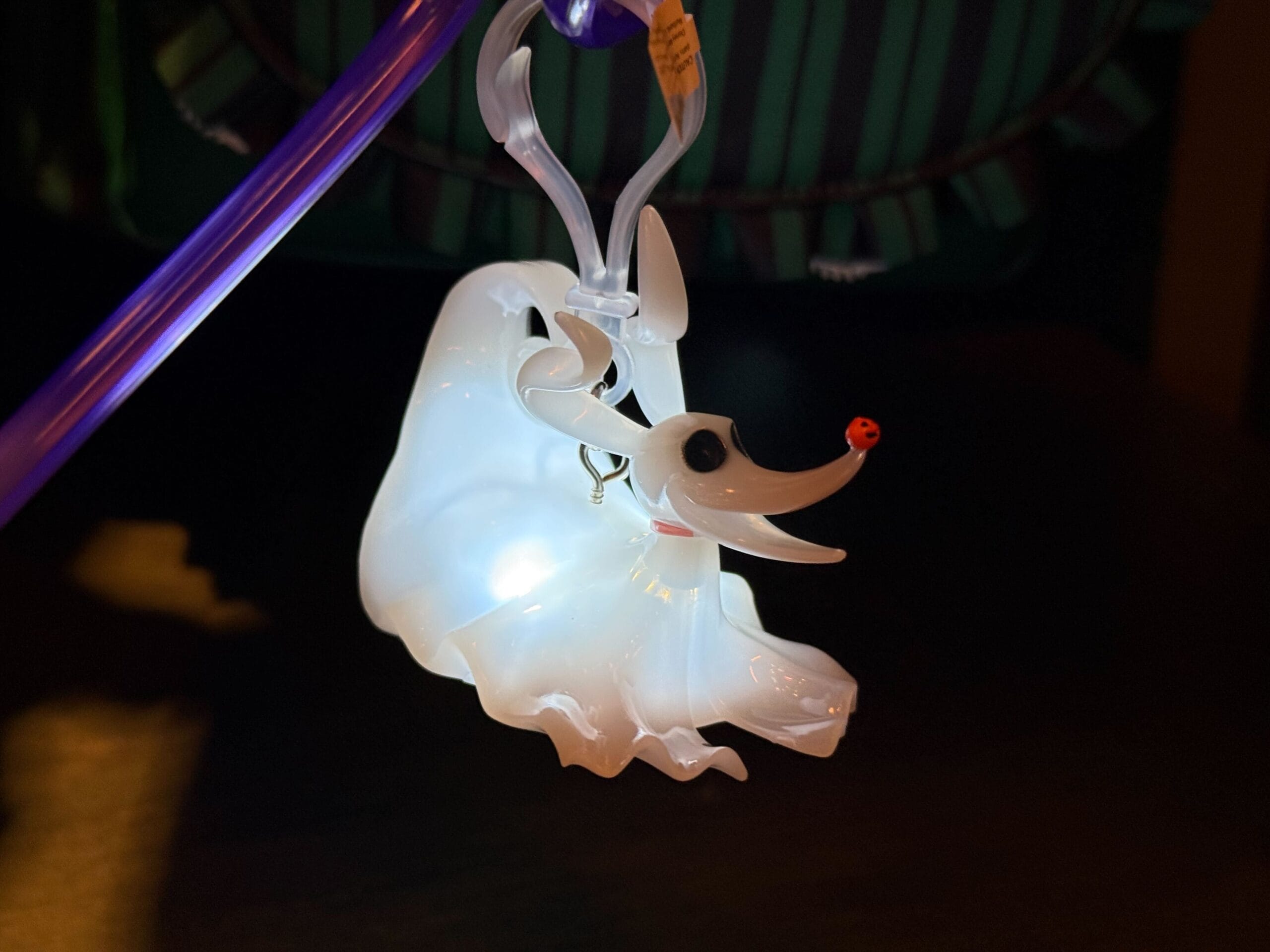 A glowing glass ornament shaped like a ghostly dog with a red nose, hanging from a clear hook.
