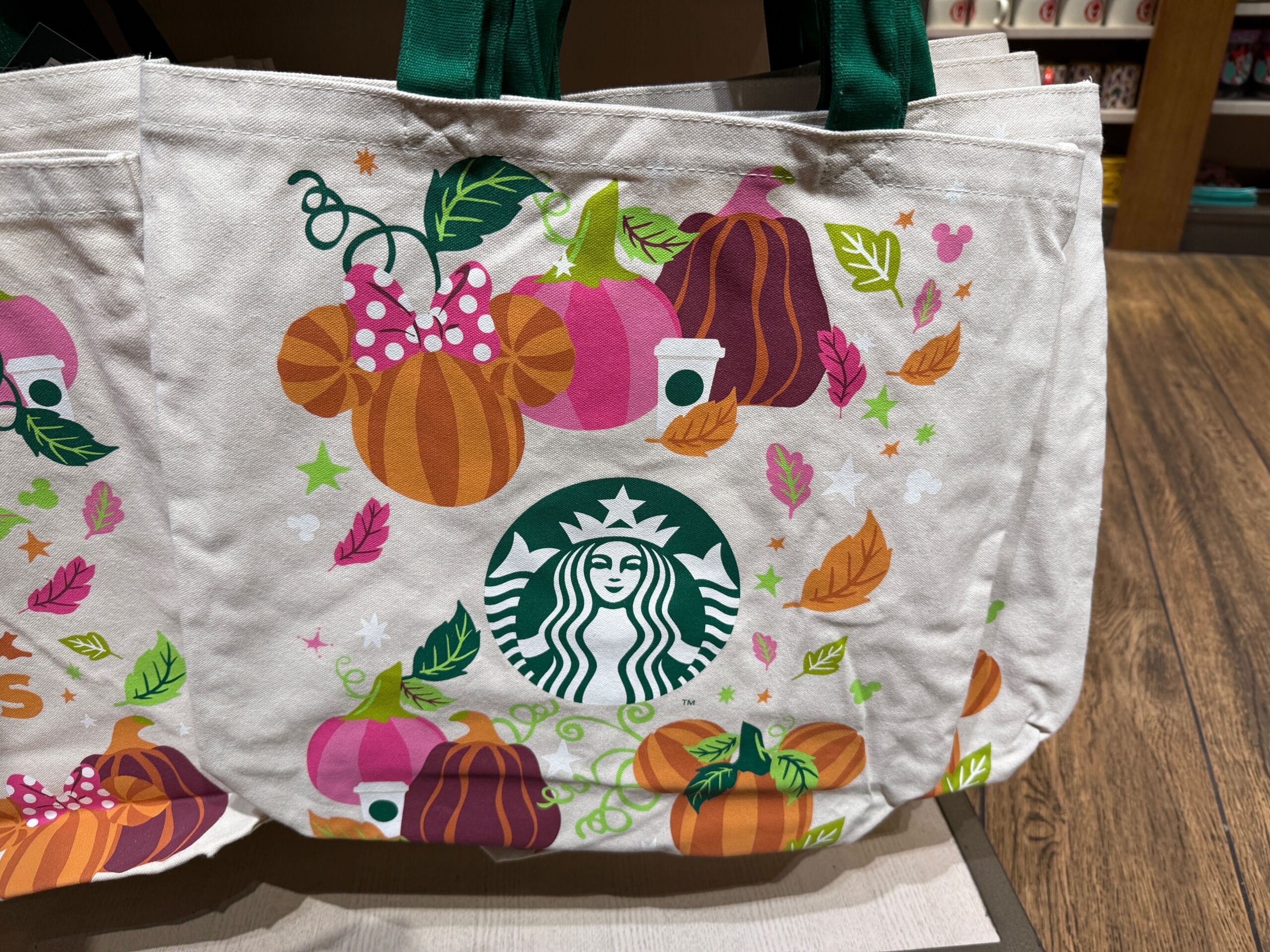 A white Starbucks tote bag featuring colorful pumpkins, leaves, and the green Starbucks Pumpkin Spice logo in the center.