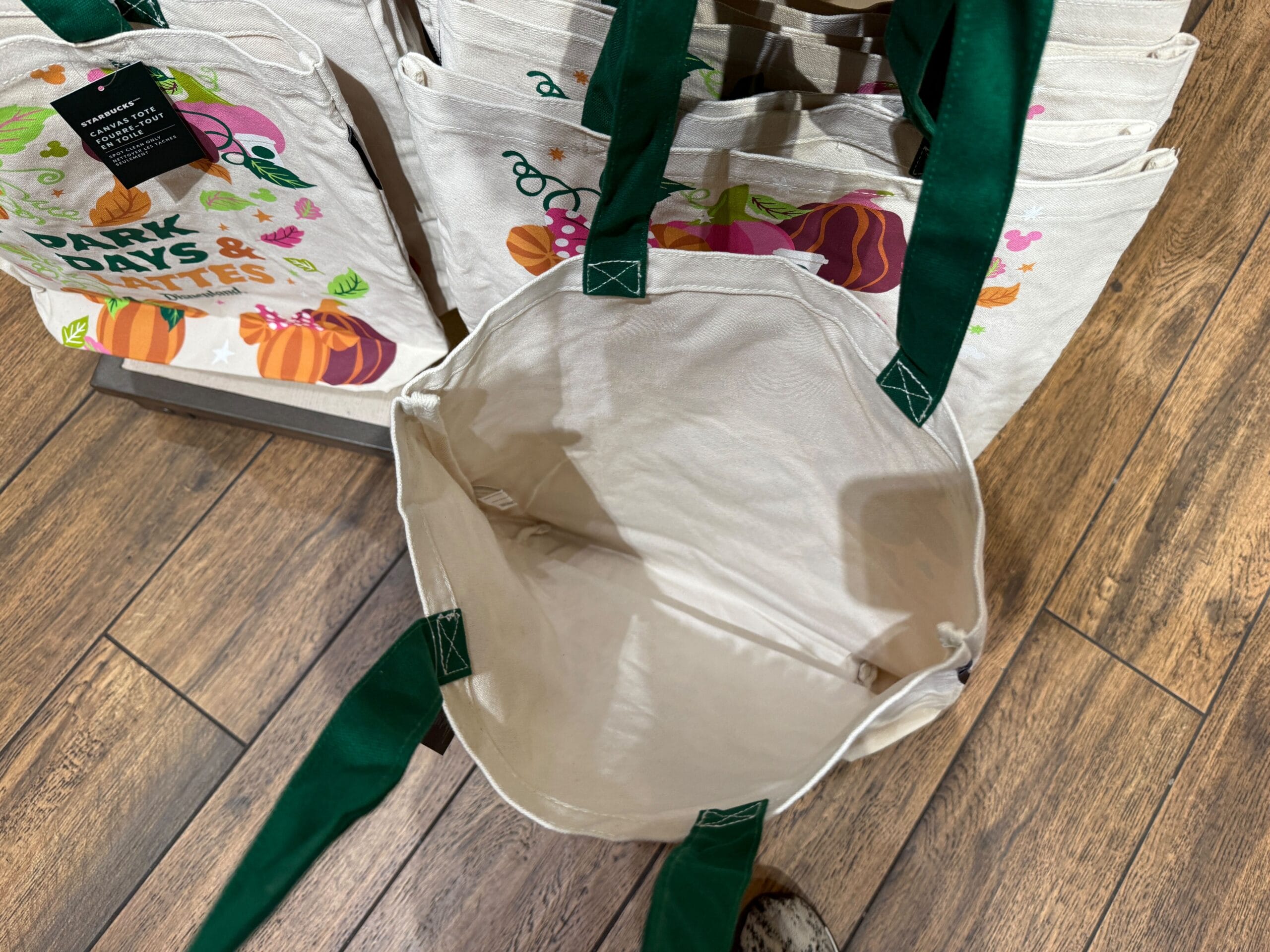 A fabric tote bag with green handles, like those at Disneyland Resort, displayed open on a wooden floor.