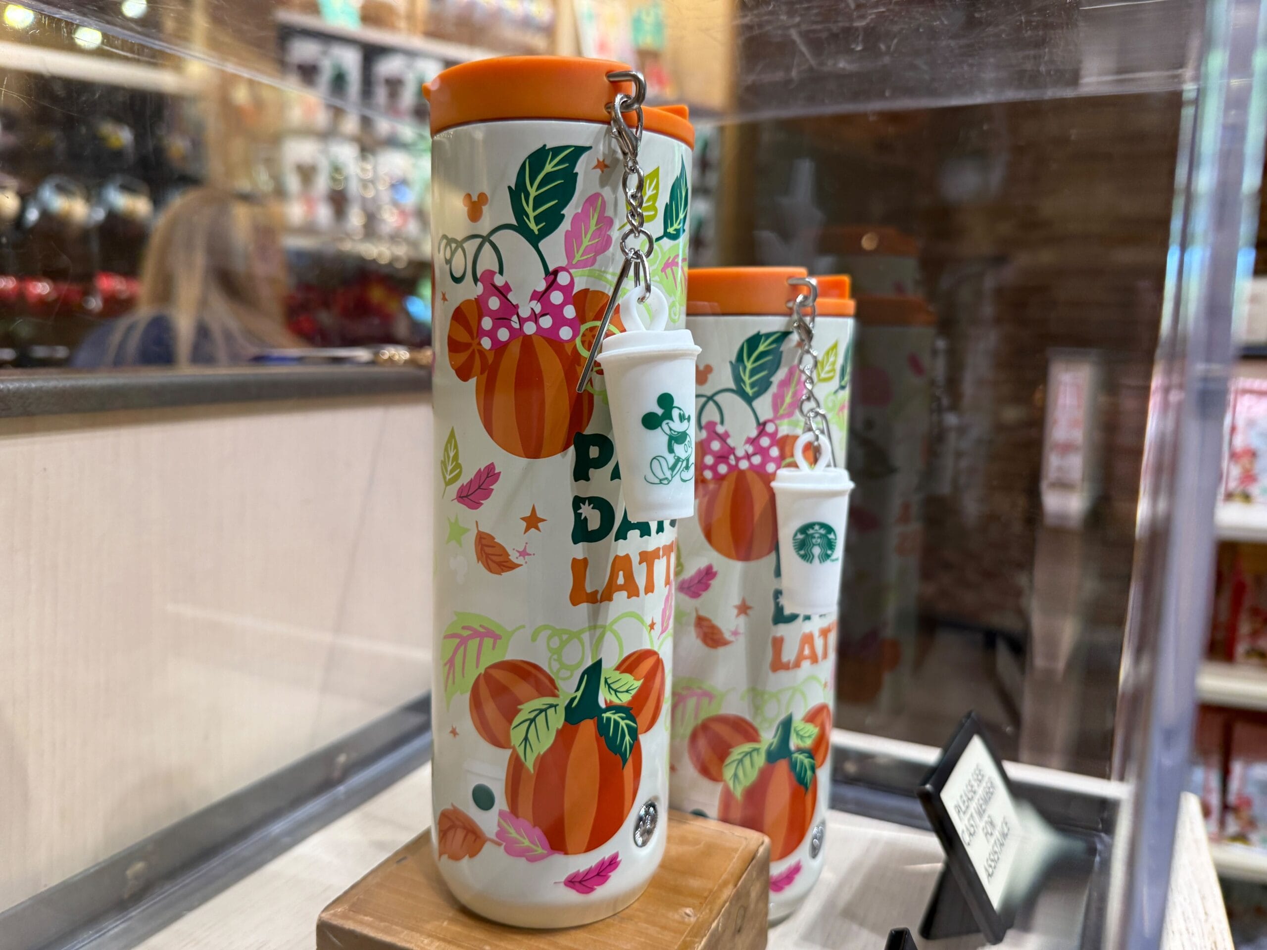 Starbucks Pumpkin Spice Merchandise tumblers with orange lids and keychains displayed on a wooden stand.