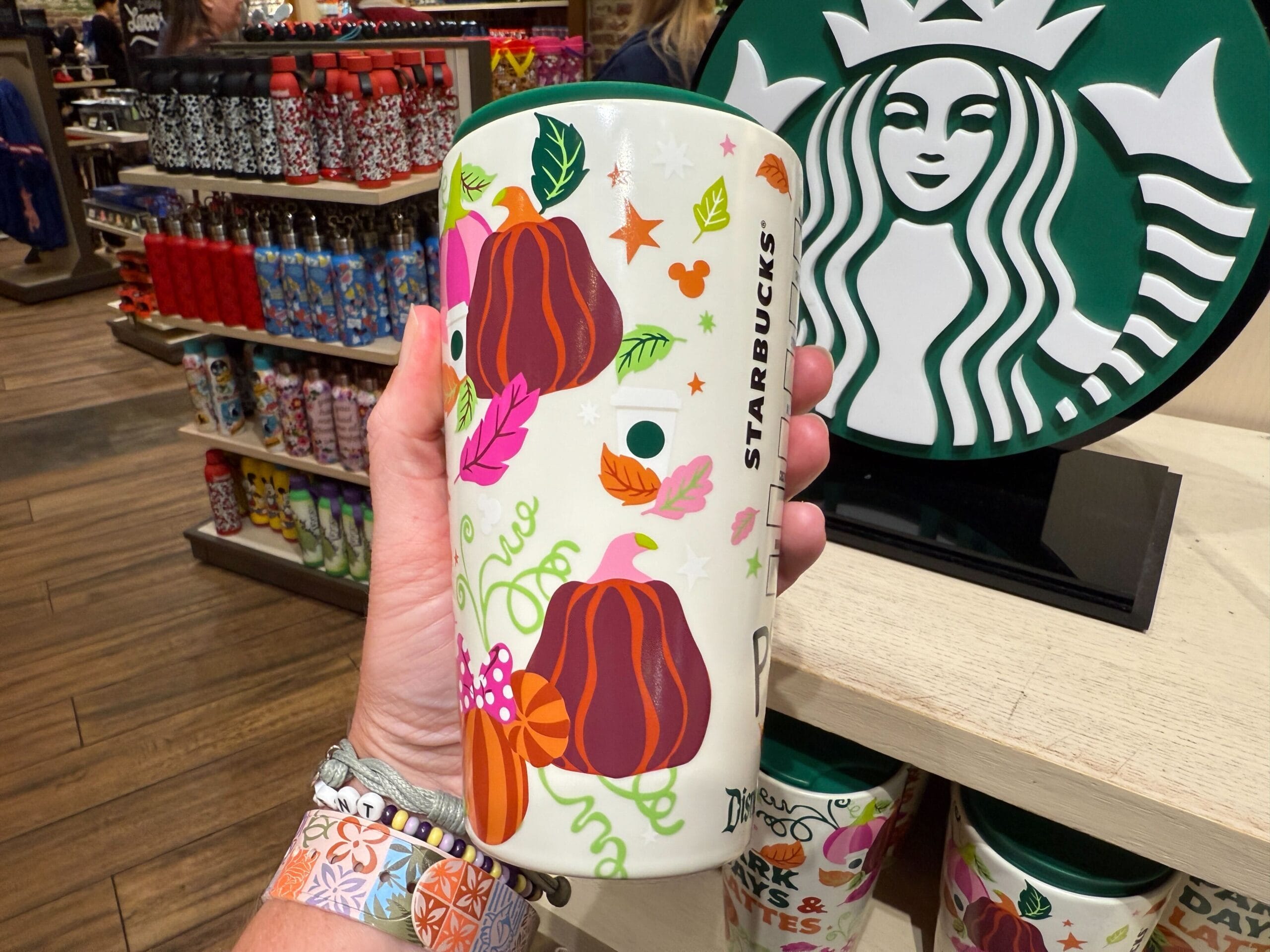 A hand holds a Starbucks Pumpkin Spice tumbler with pumpkins and leaves at a store, perfect for Disneyland Resort fans.