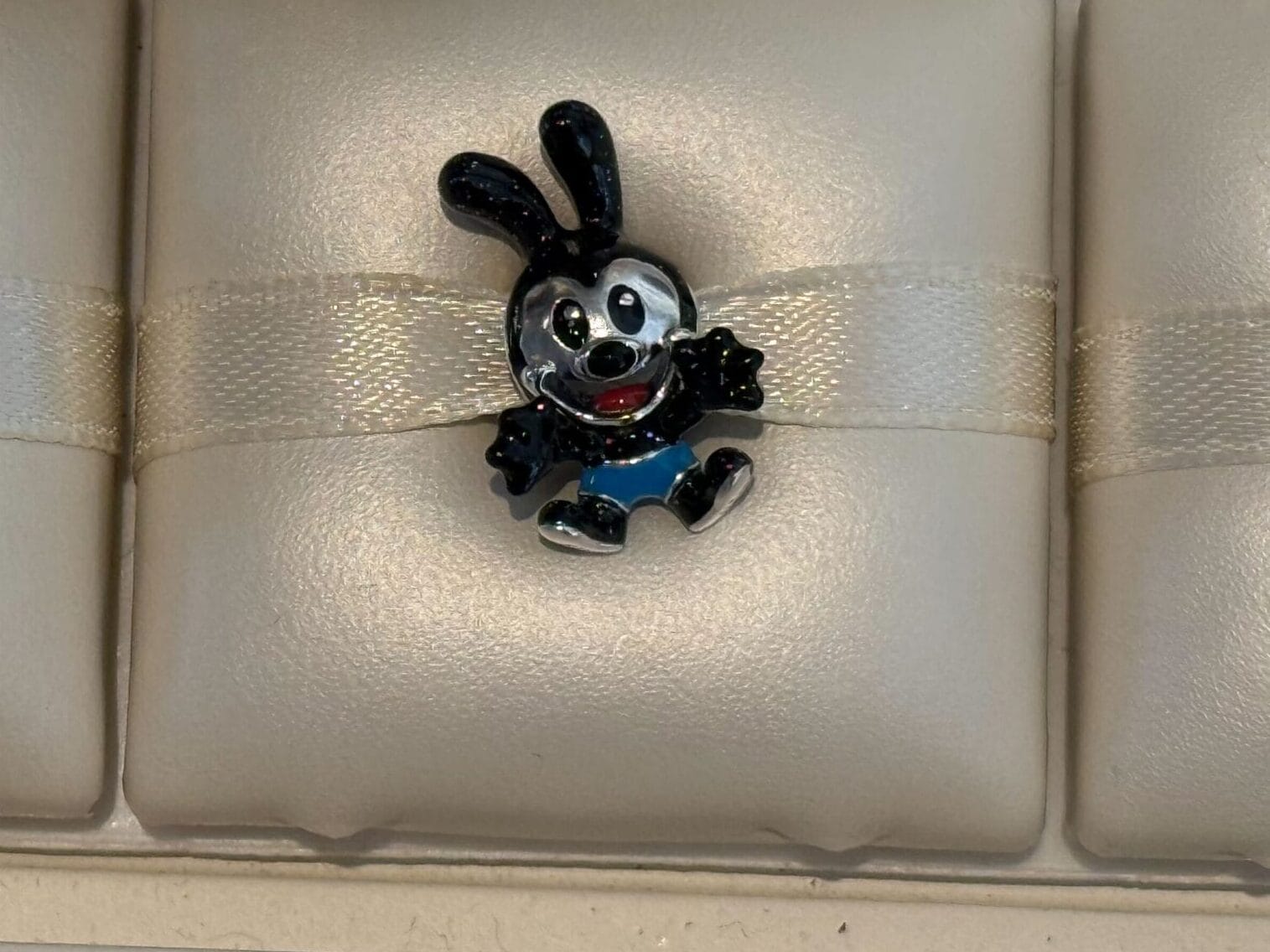 New Pandora Charms featuring Olaf the snowman and Oswald the Lucky Rabbit, displayed on cream-colored cushions.