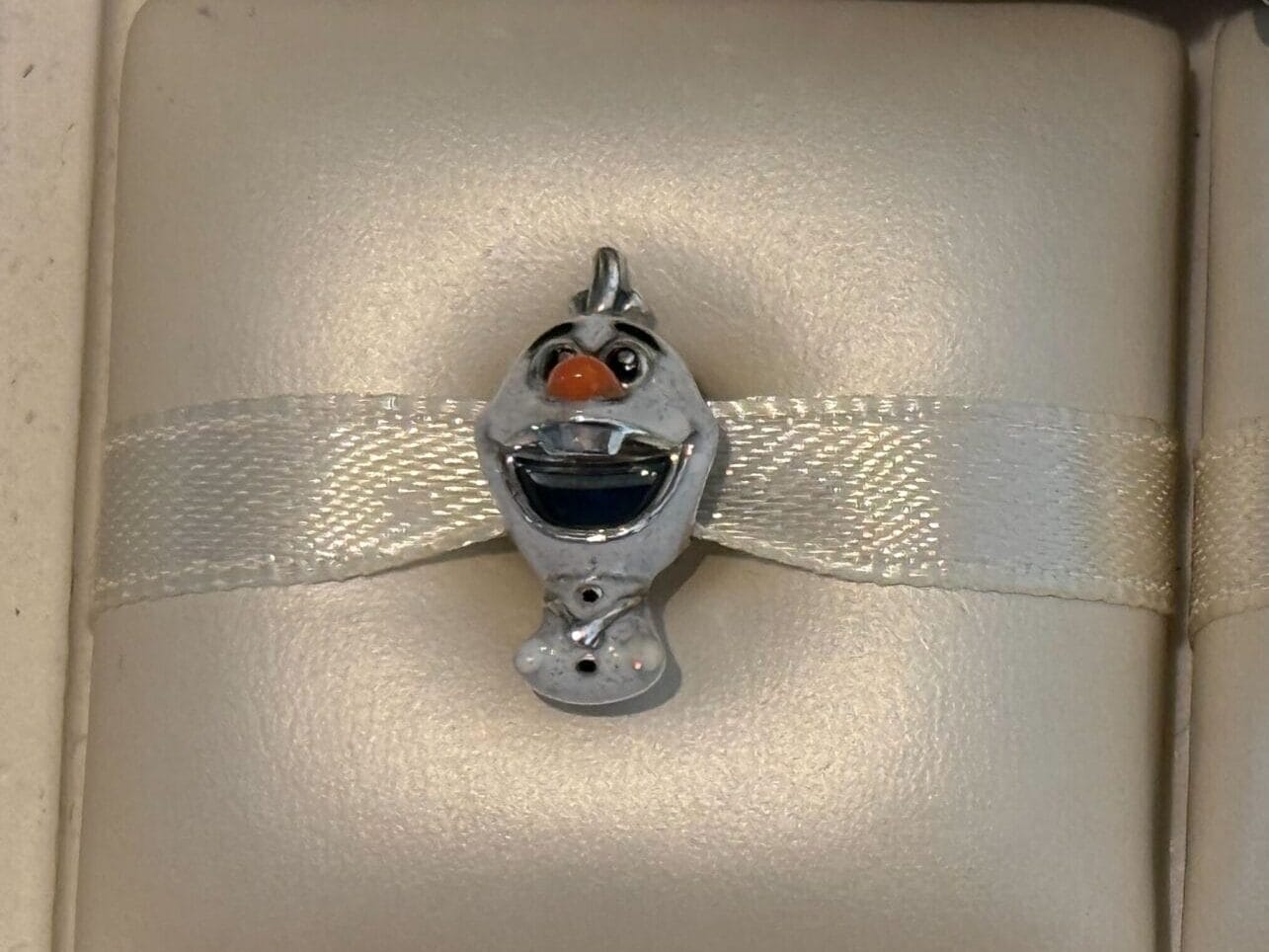 Two cartoon character Pandora Charms, Olaf and Oswald, displayed on cream-colored holders.
