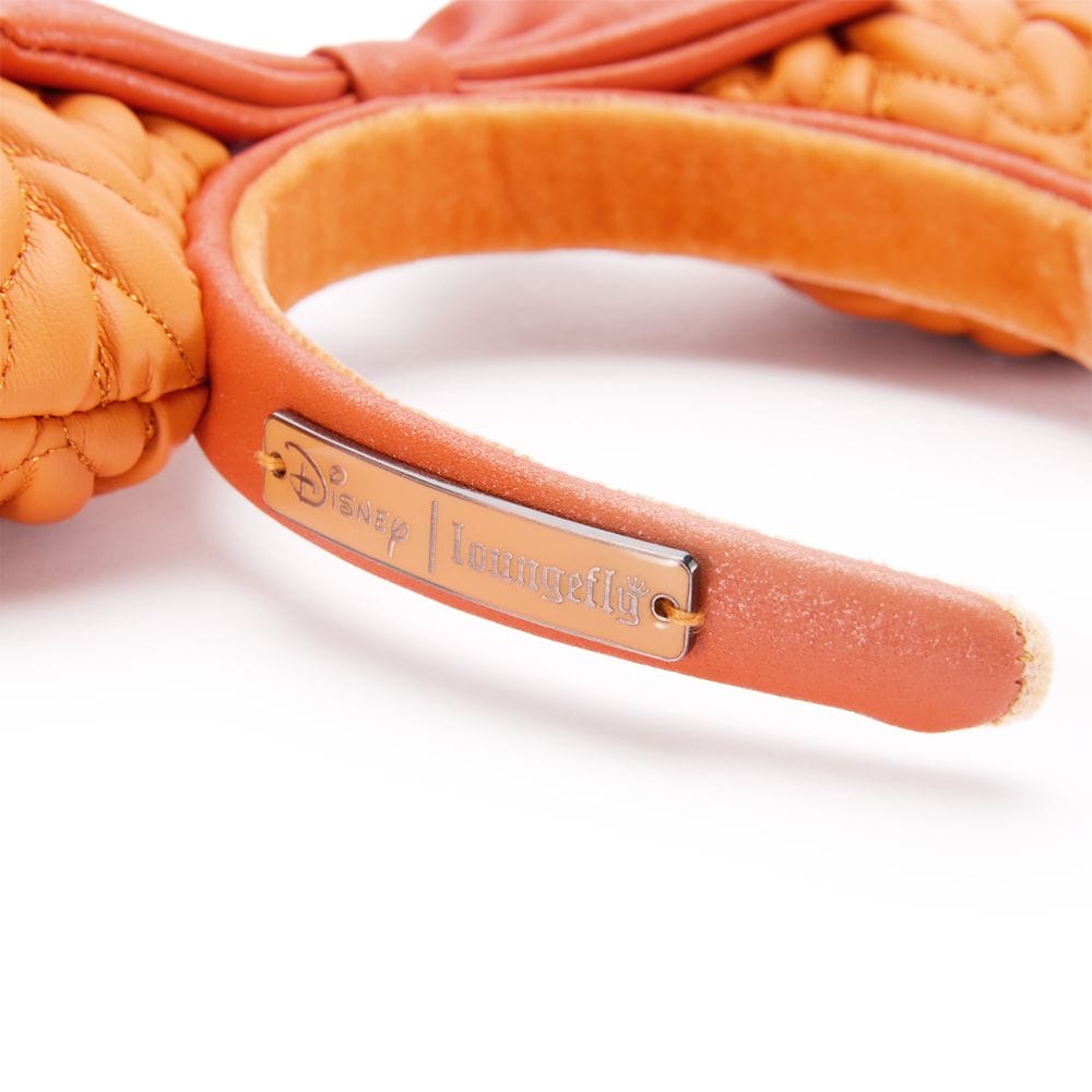 Close-up of an orange Disney x Loungefly headband from the Pumpkin Spice Collection with a metal logo plate on the side.