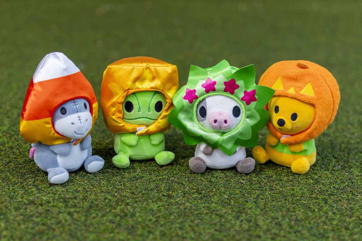 Four Mini MixIts in colorful costumes—a rocket, leaf, flower, and cat—sit on green grass.