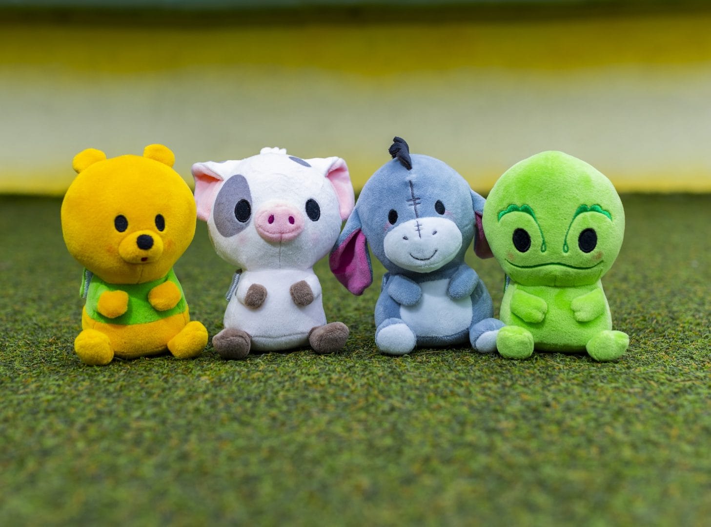 Four cute Mini MixIts plush toys—a bear, pig, donkey, and chameleon—sit in a row on green grass.