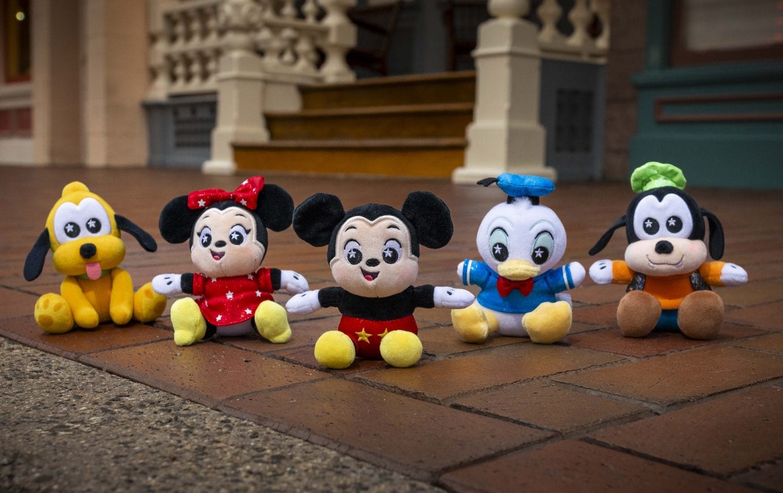 Five Disney Shimmer Wishables plush toys sit on a brick pavement in front of a building.