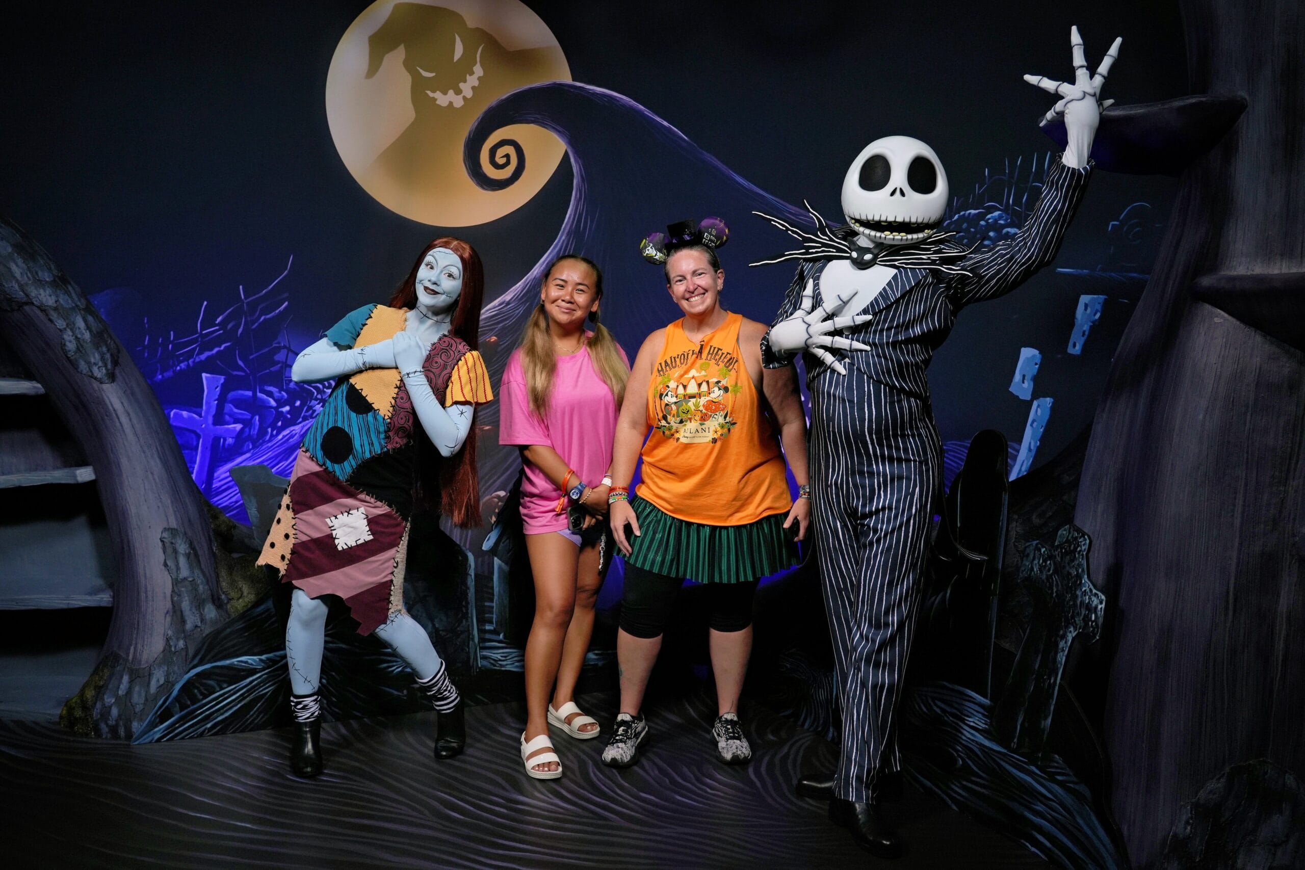 Two women pose with Sally and Jack Skellington at a spooky backdrop during Mickey's Not So Scary Party.