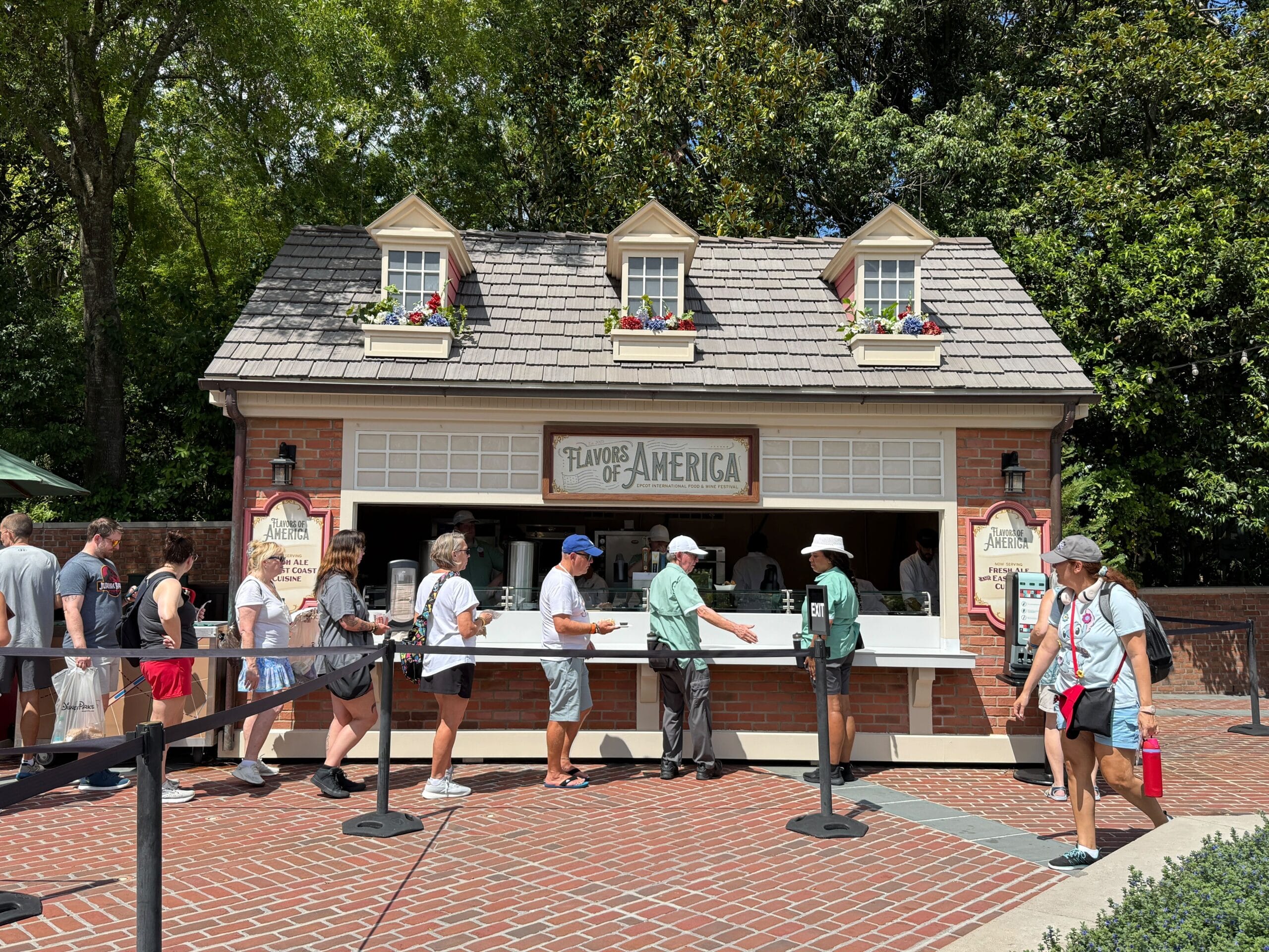 People line up at the "Flavors of America" food stand, enjoying a sunny Food & Wine event.