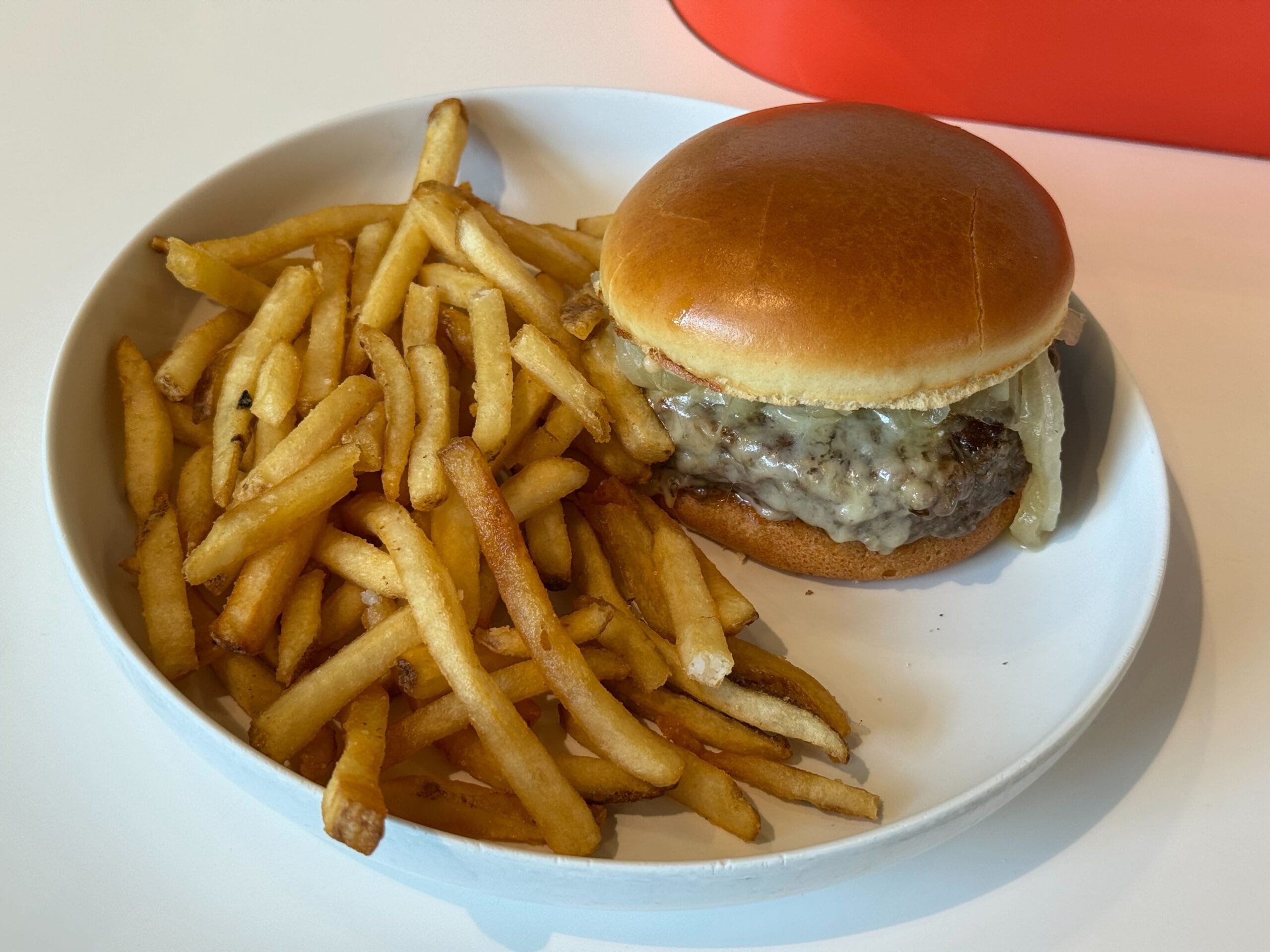 A plate with a cheeseburger in a brioche bun and French fries, featured at New Food & Wine, on a white table.