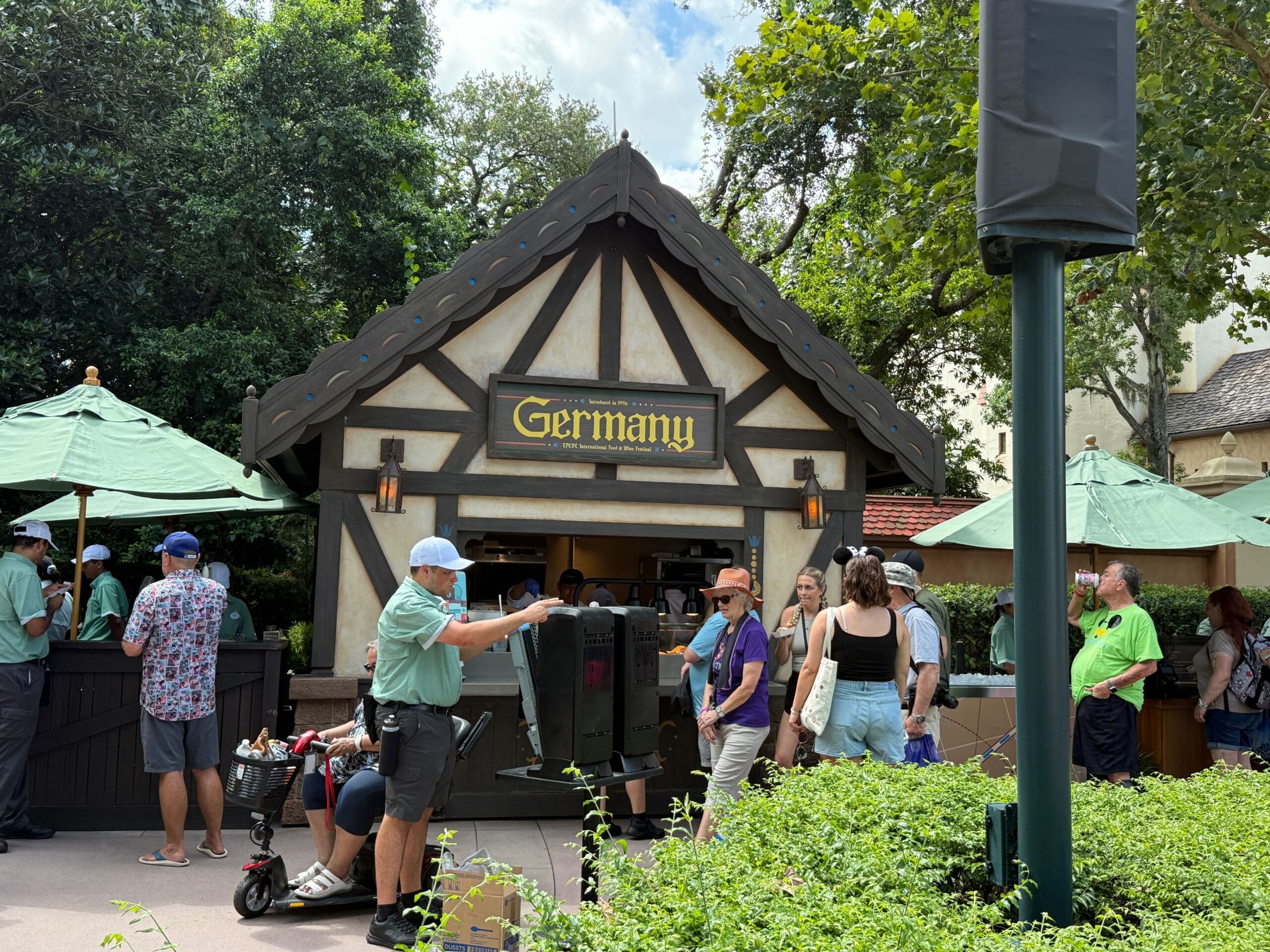 A group stands before a Germany-themed Food & Wine kiosk with a peaked roof and a bright yellow "Germany" sign.