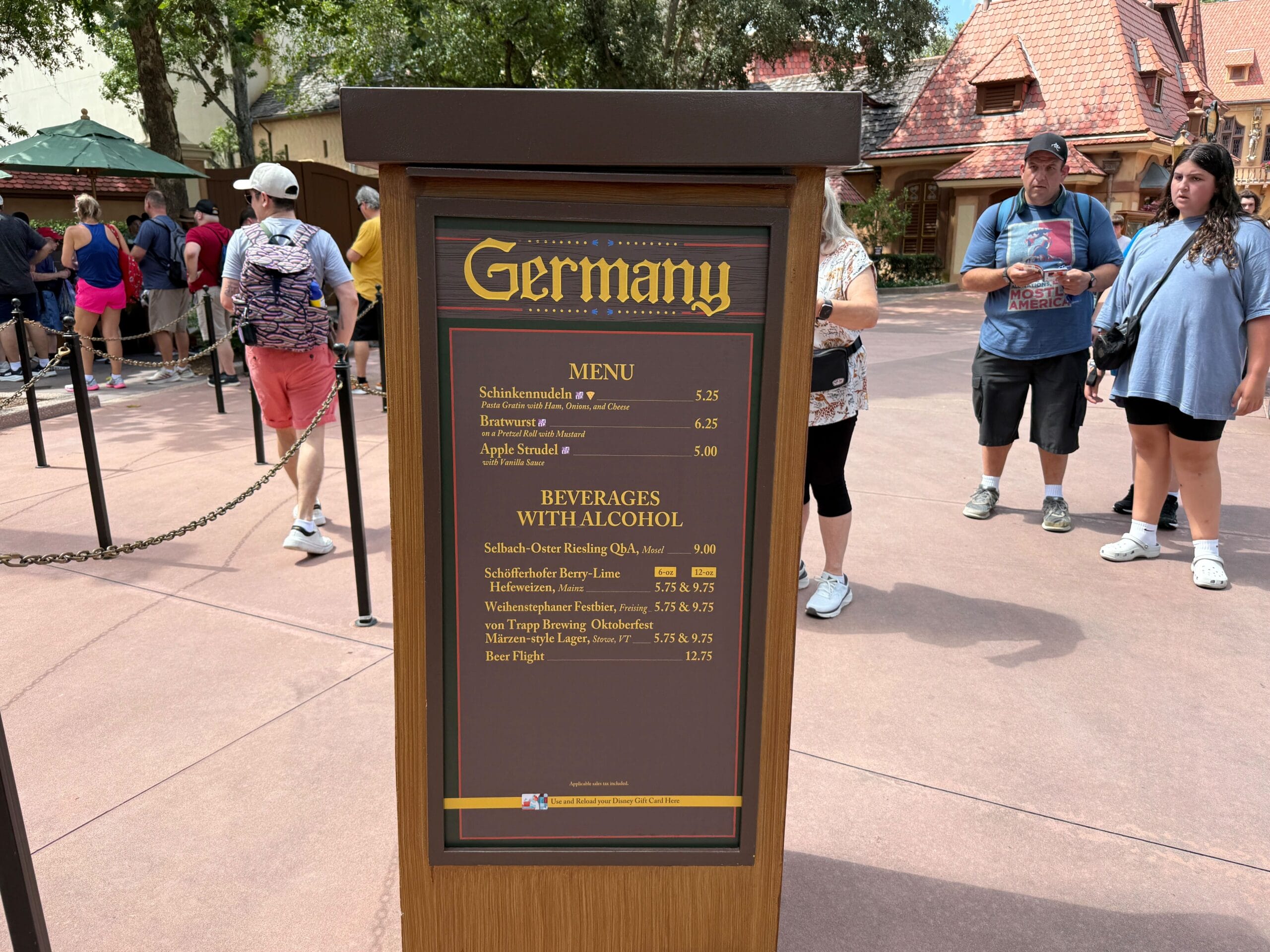 A menu outside the Germany pavilion at Epcot lists Food & Wine options; people stand nearby.