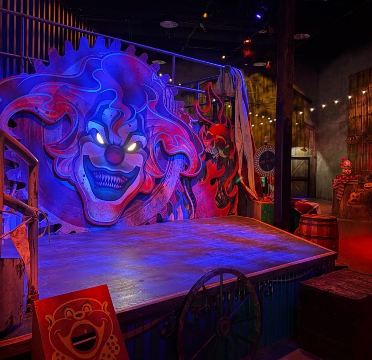 FIRST LOOK: A stage with a large, glowing, sinister clown face backdrop amid carnival and circus-themed props at Universal Horror Unleashed.