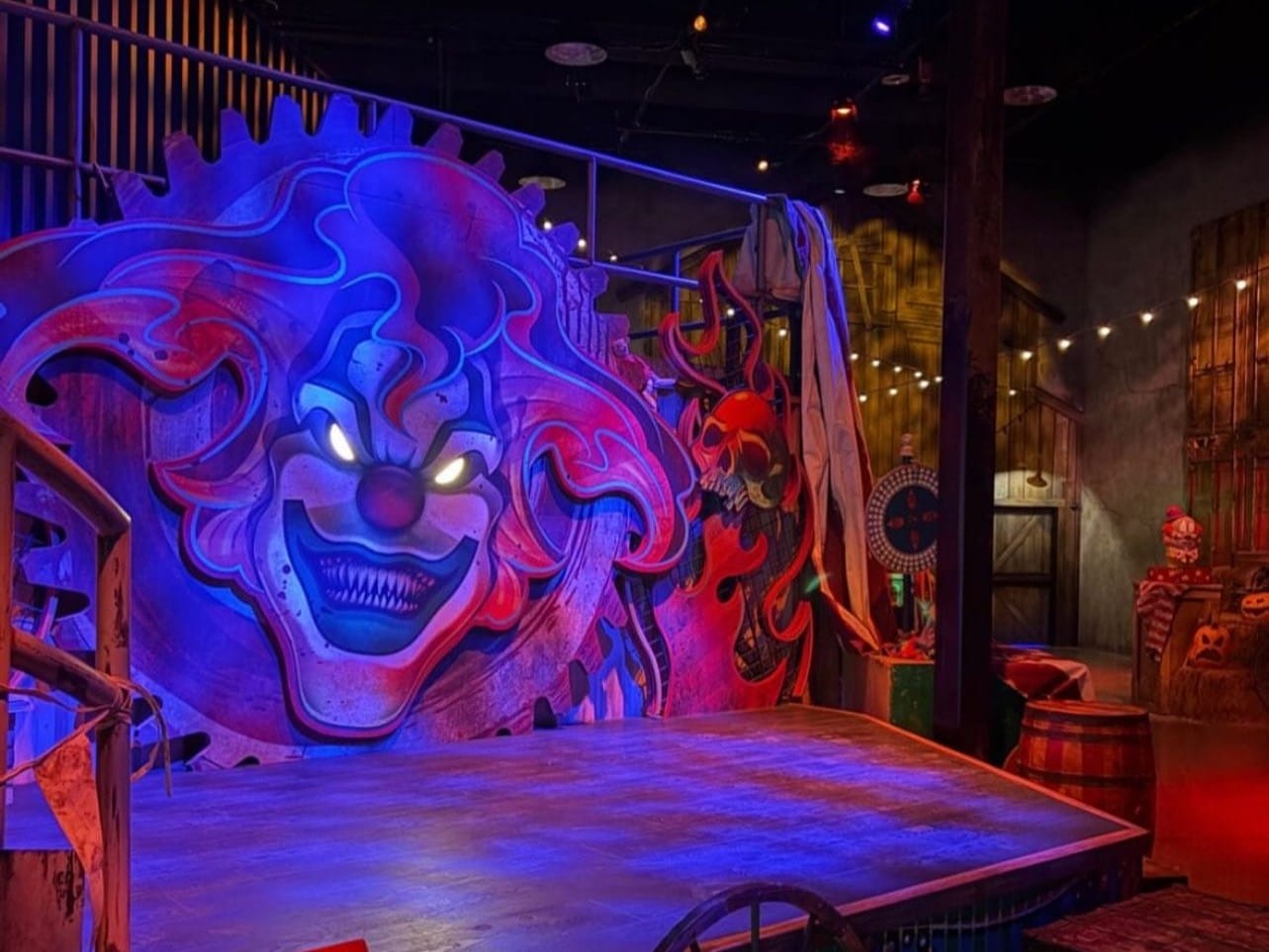 A creepy clown face mural with glowing eyes haunts a Las Vegas carnival stage at Universal Horror Unleashed.