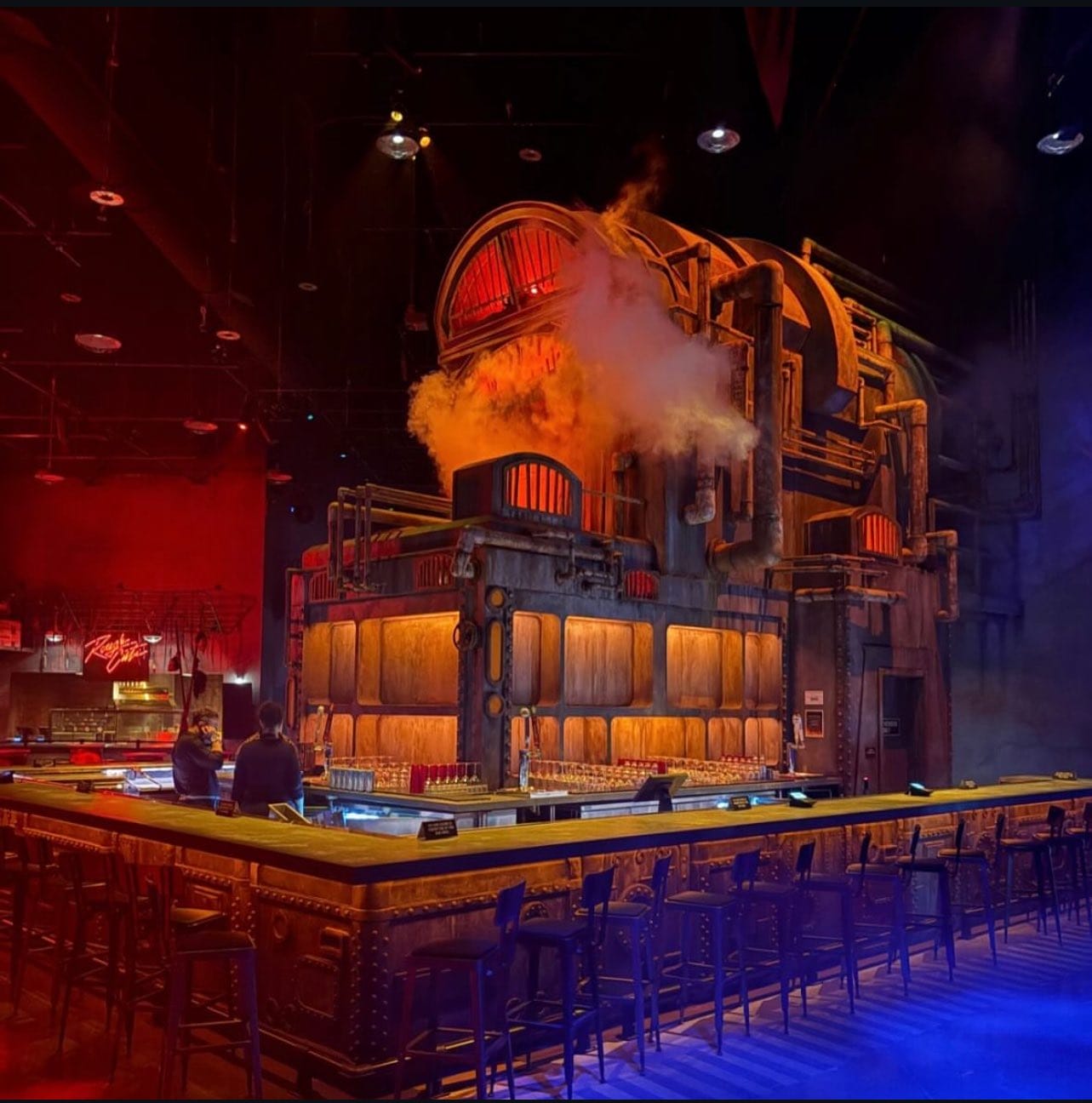 FIRST LOOK: A large, industrial-themed bar with glowing orange lights and a dramatic steampunk-style machine centerpiece at Universal Horror Unleashed.