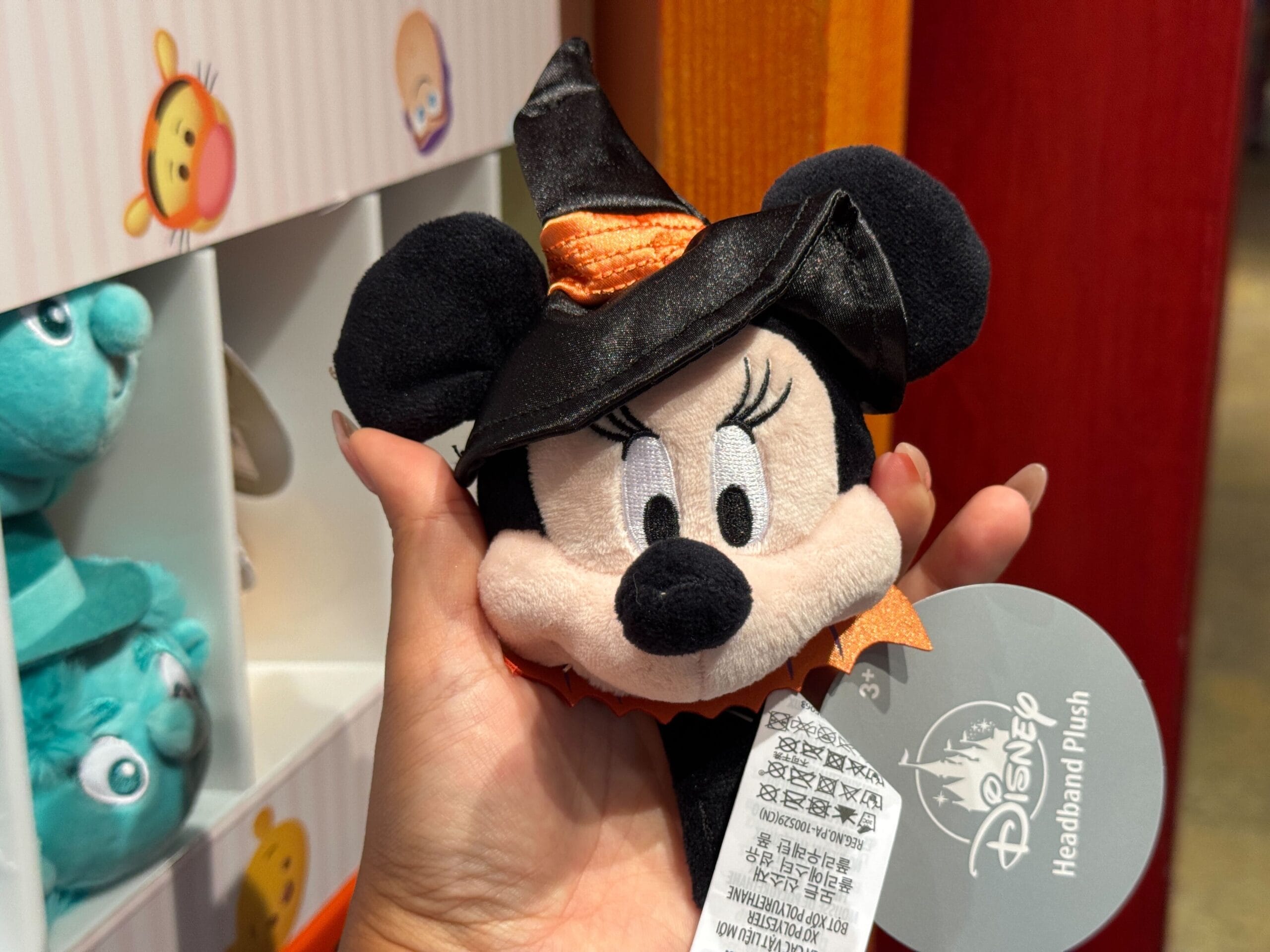 A hand holds a plush Minnie Mouse Halloween merchandise headband with a witch hat in a Disney store.