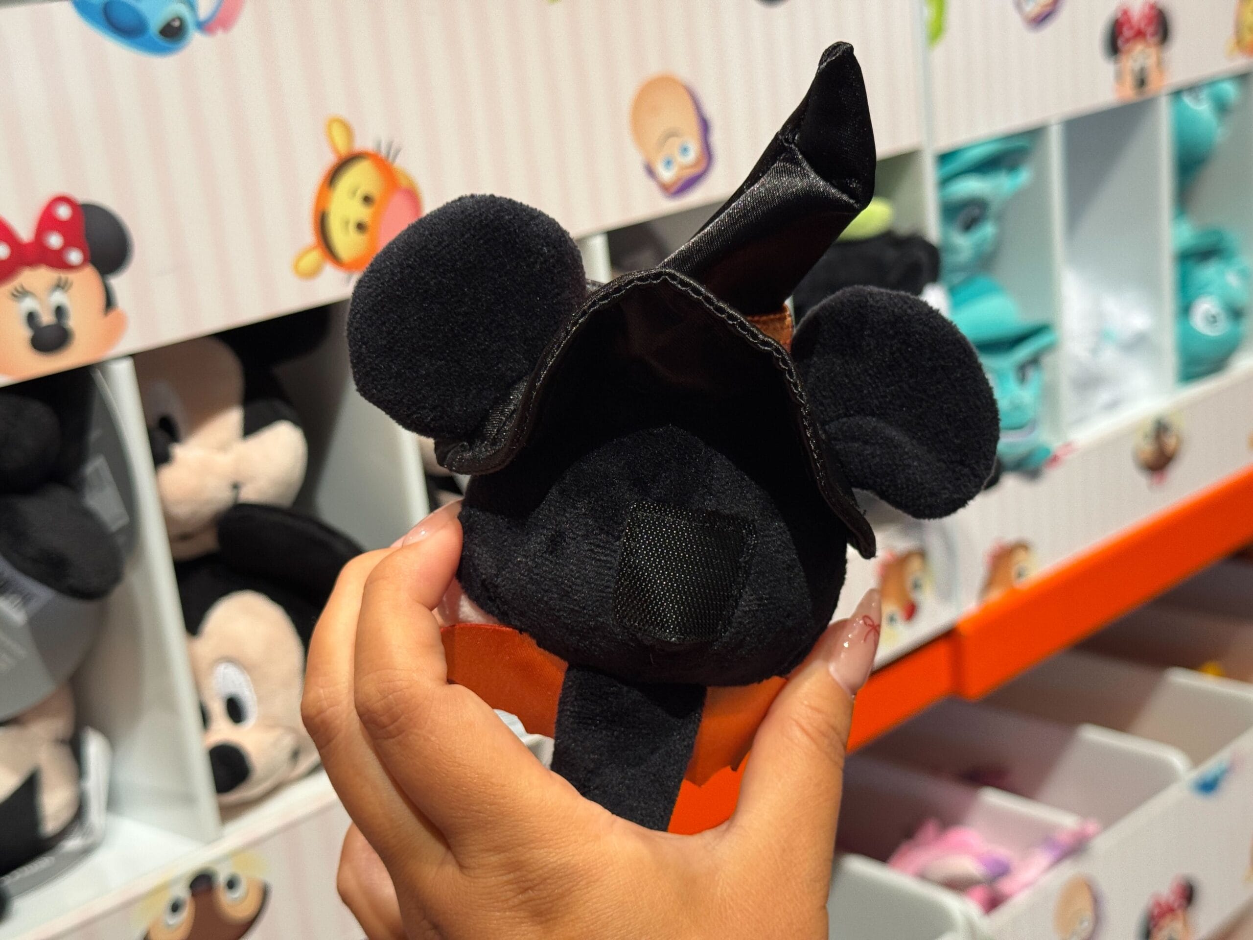 A hand holds a small plush Mickey Mouse toy in a black witch hat, part of the Halloween Merchandise at Walt Disney World.