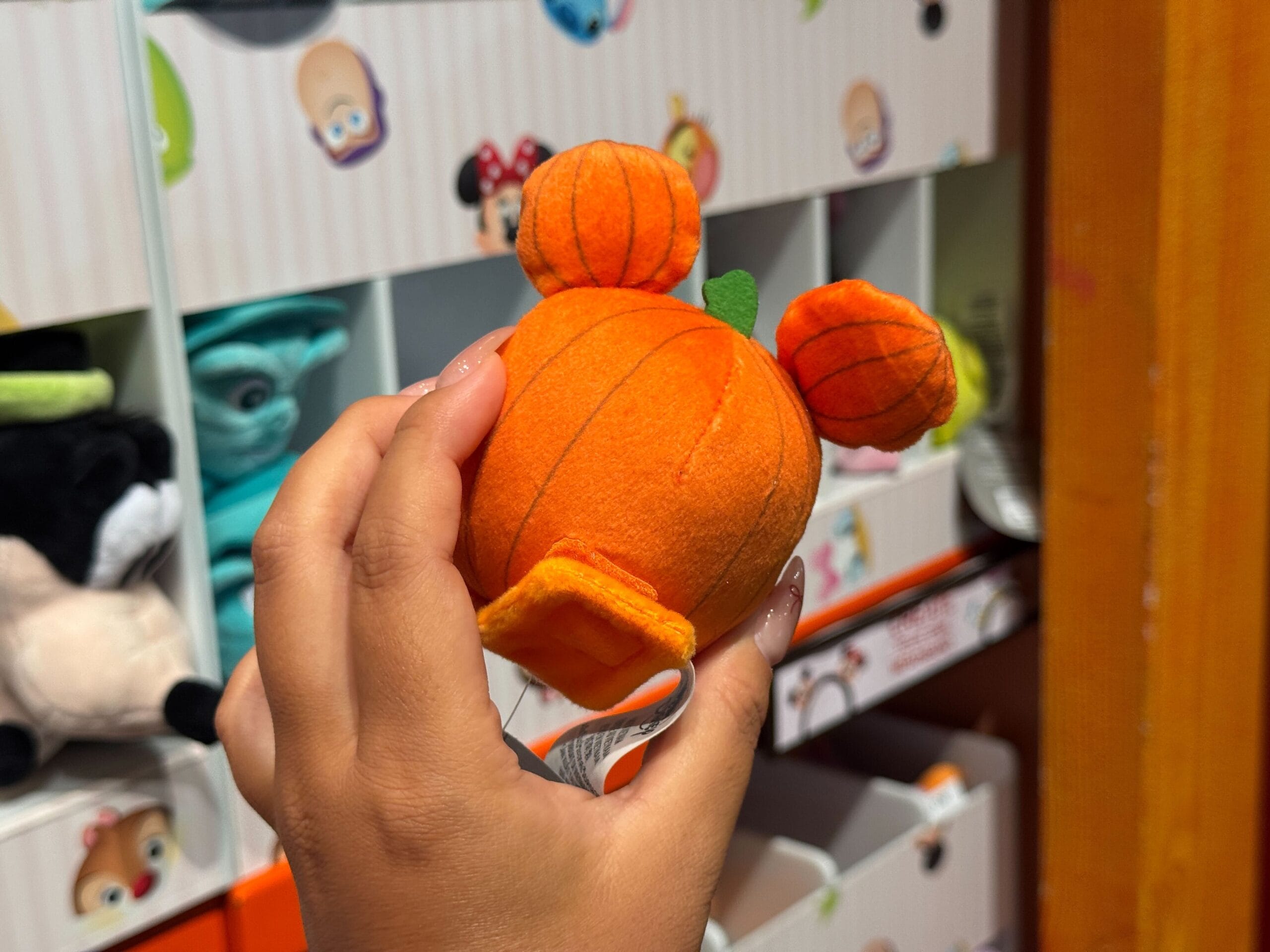A hand holds a small plush pumpkin with mouse ears—cute Halloween merchandise found in a Walt Disney World store display.