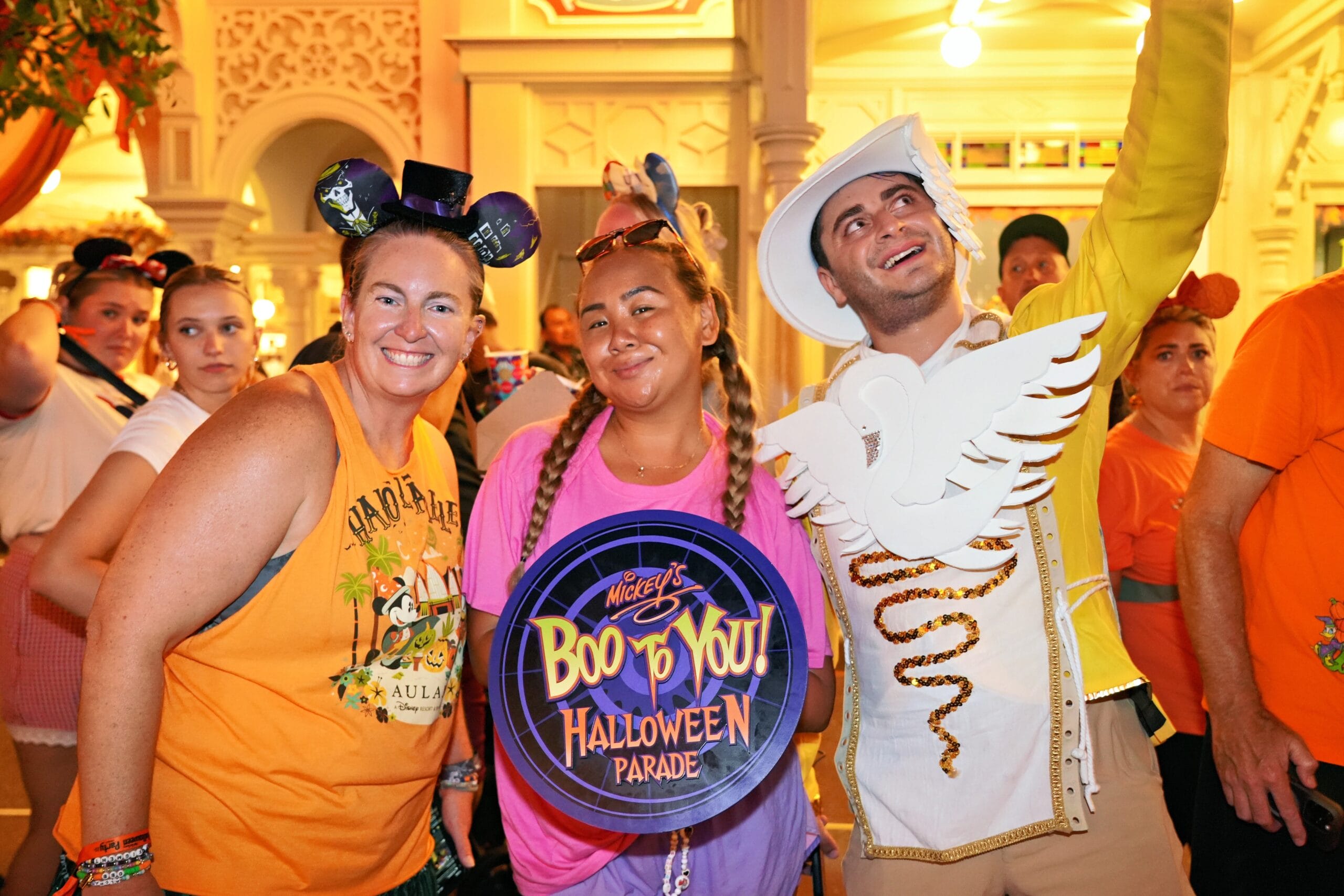 Three people in Halloween costumes smile at Mickey's Not So Scary Party, a festive event with others in the background.