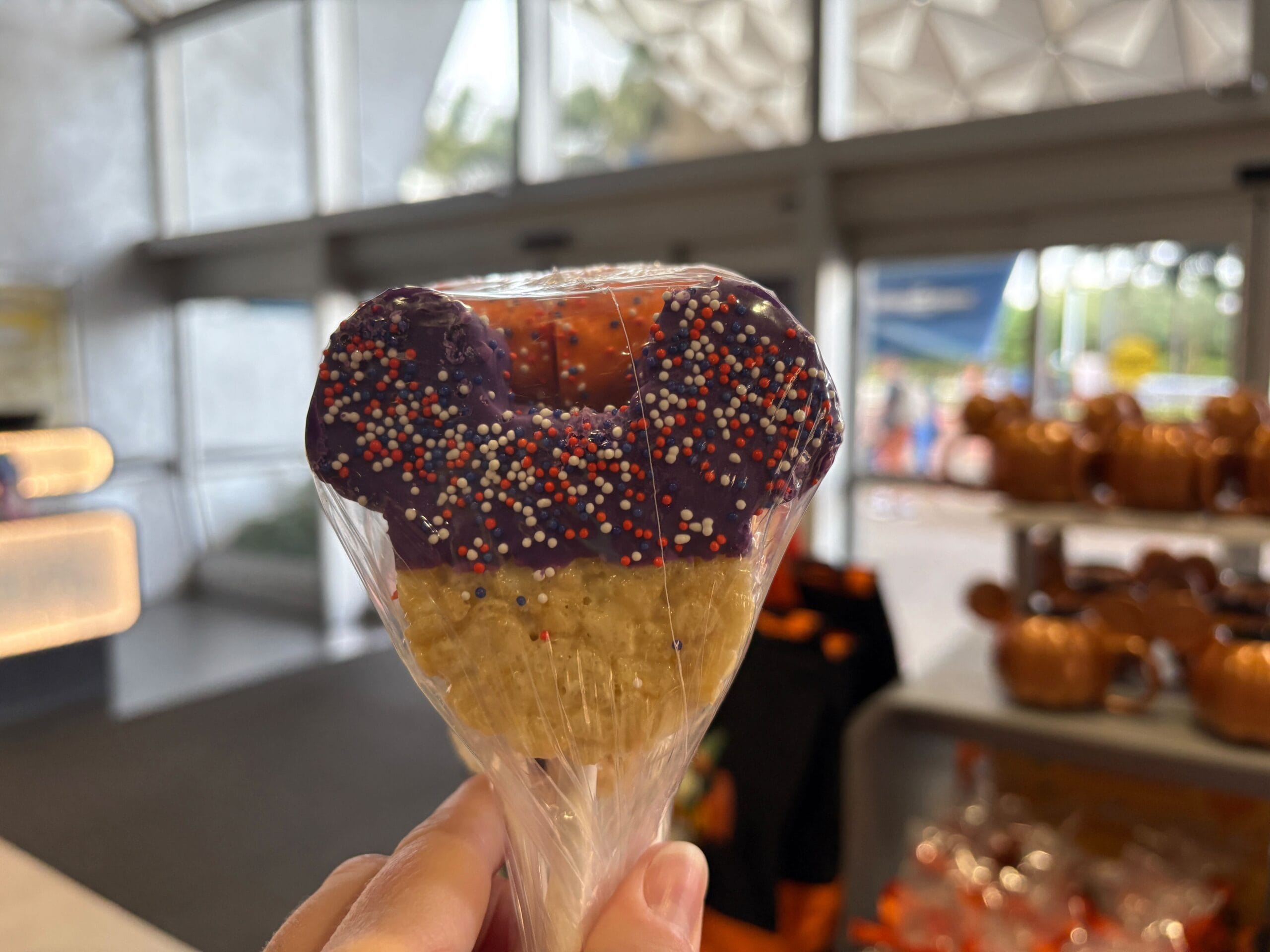 A hand holds a Mickey-shaped Rice Krispies treat with purple icing—fresh Disney Halloween Merch at Walt Disney World.