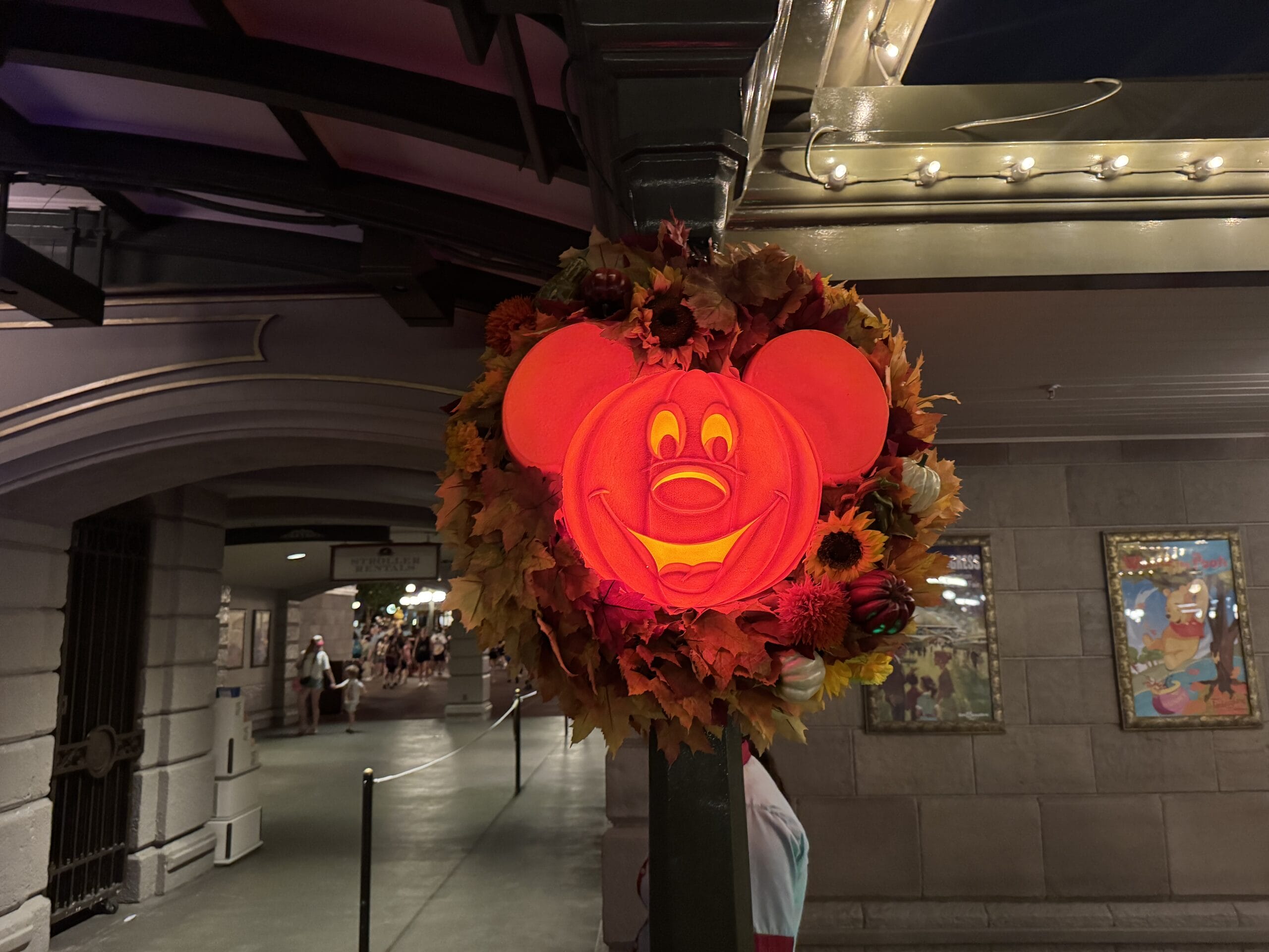 A glowing Mickey Mouse pumpkin shines on a lamppost at night during Mickey's Not So Scary Party in the theme park.