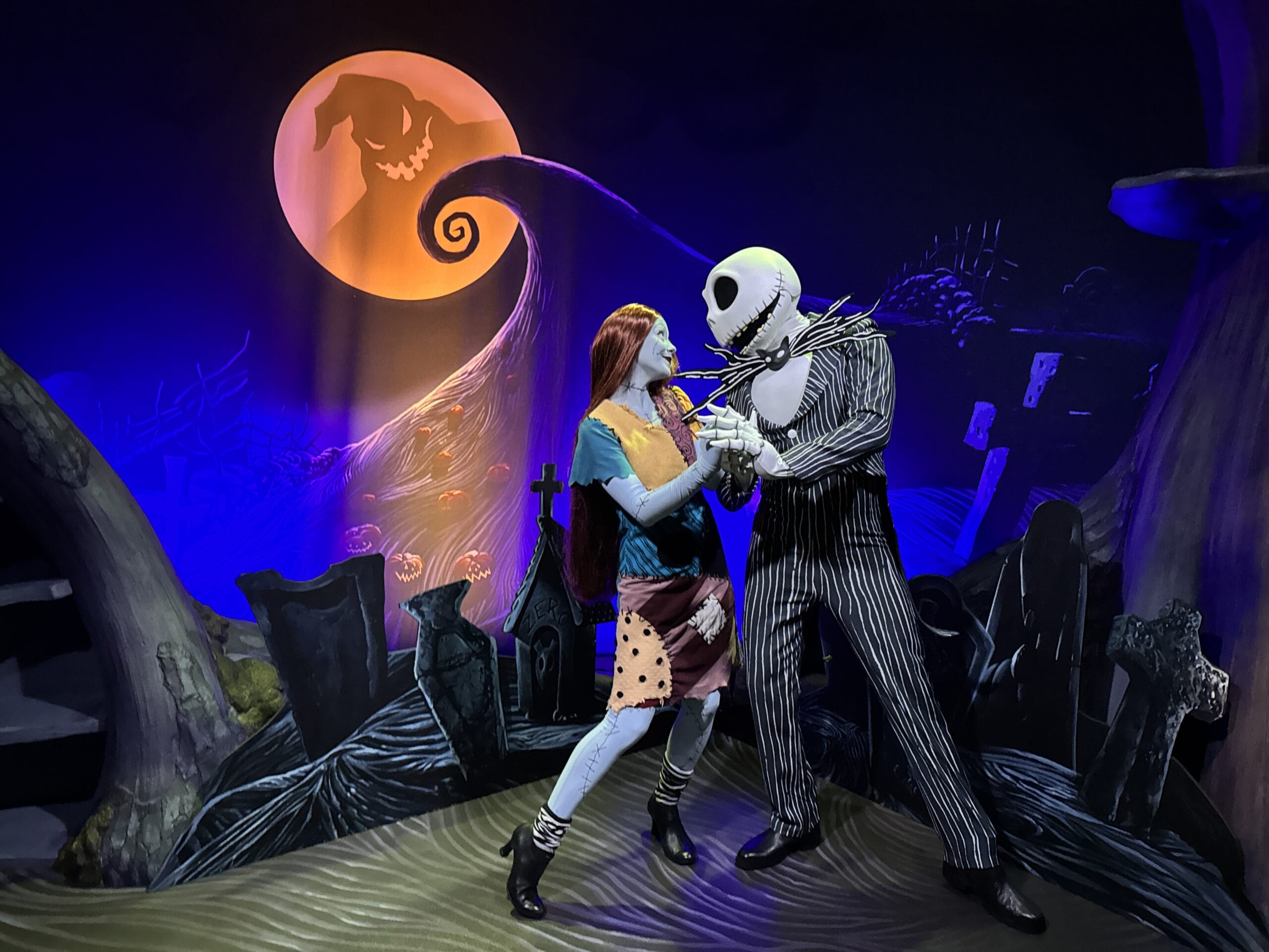 Jack Skellington and Sally dance under a glowing moon, evoking Oogie Boogie Bash in a stylized graveyard scene.