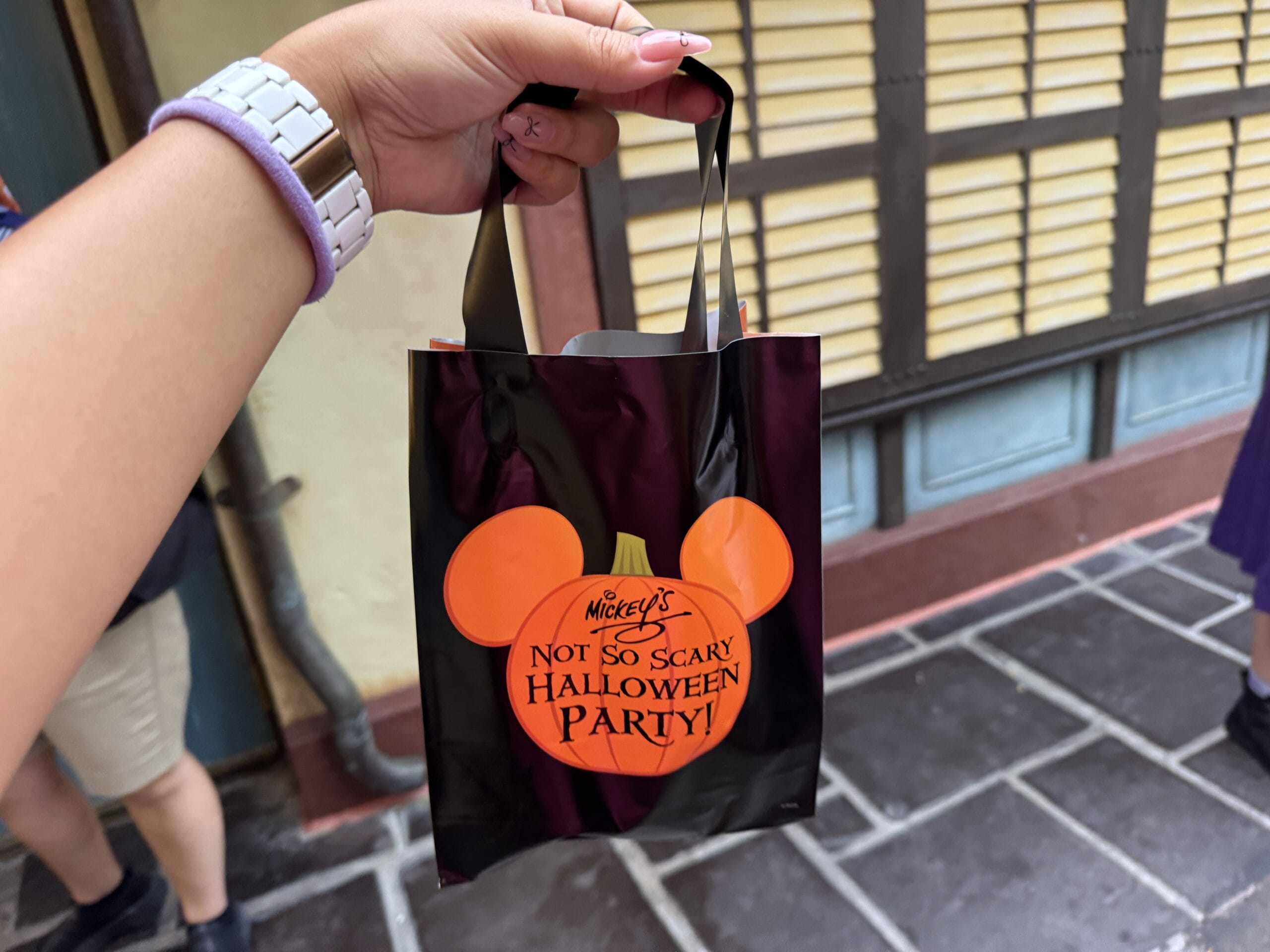 Hand holding a Mickey's Not So Scary Party treat bag, with a building background—perfect for your photo report!