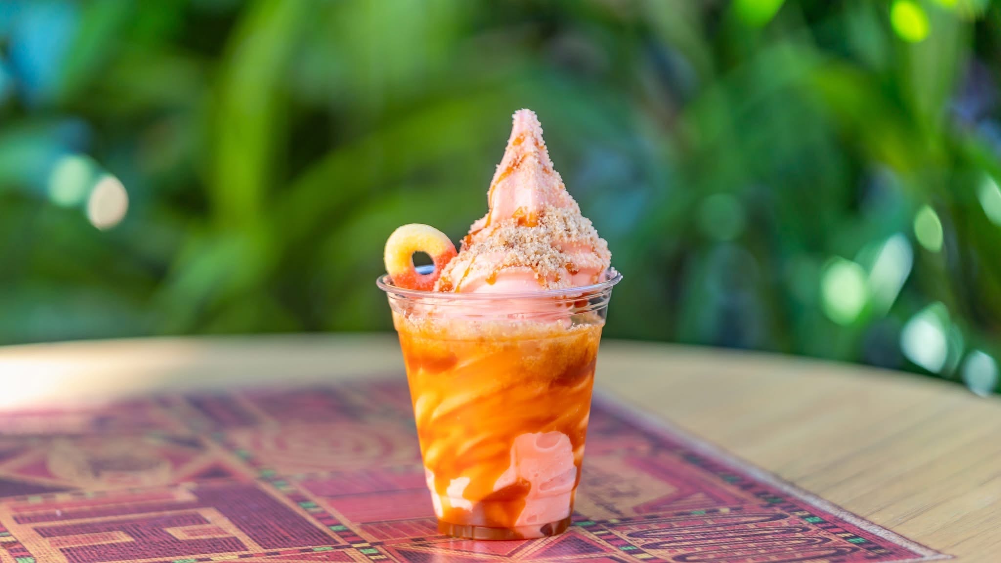A cup of soft serve ice cream with caramel sauce and a cookie, like a Peach Sundae at Disneyland, set on a patterned mat.