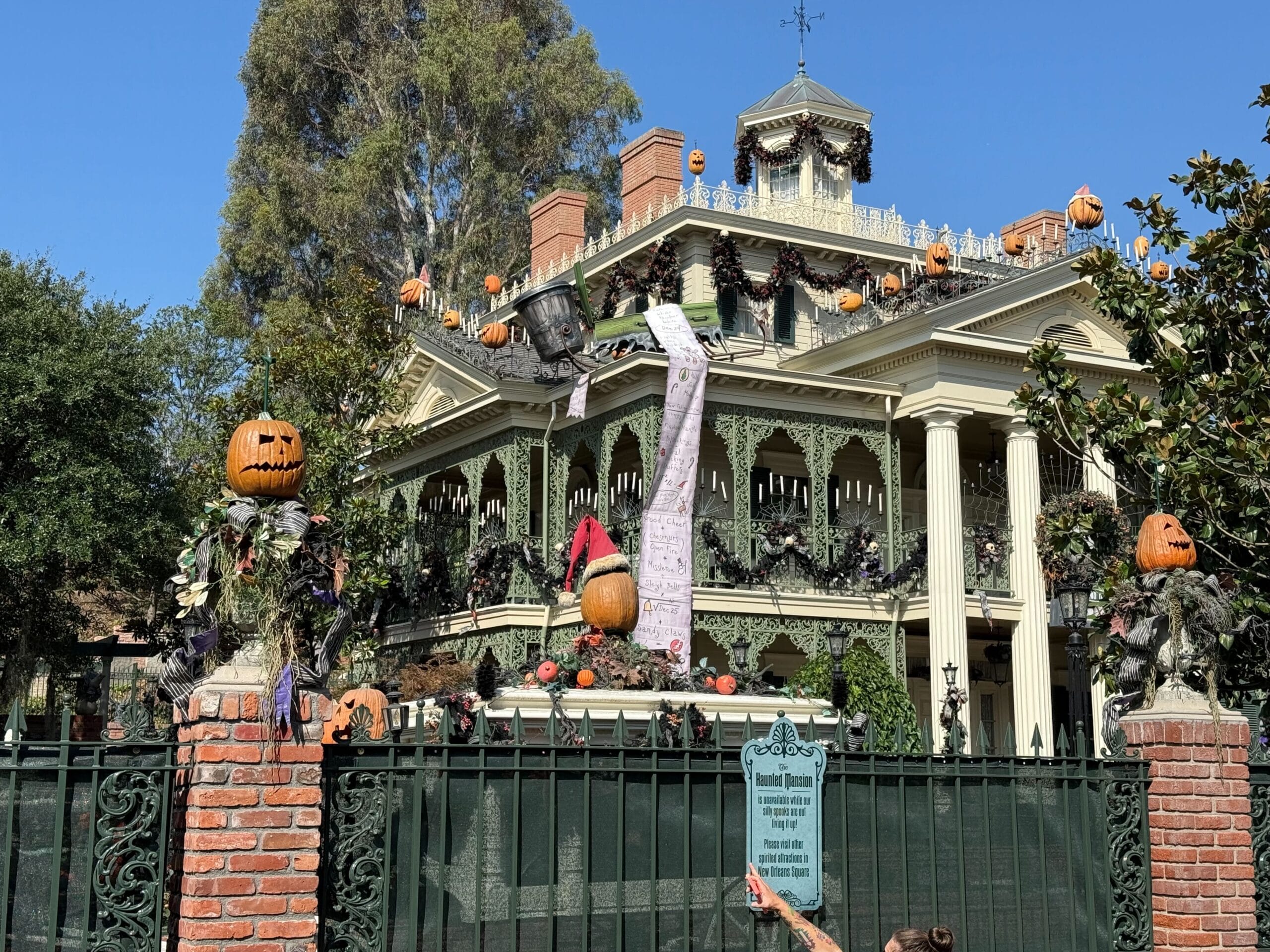 Haunted mansion at Disneyland Resort adorned with pumpkins, garlands, and Halloween Decor behind a wrought iron fence.