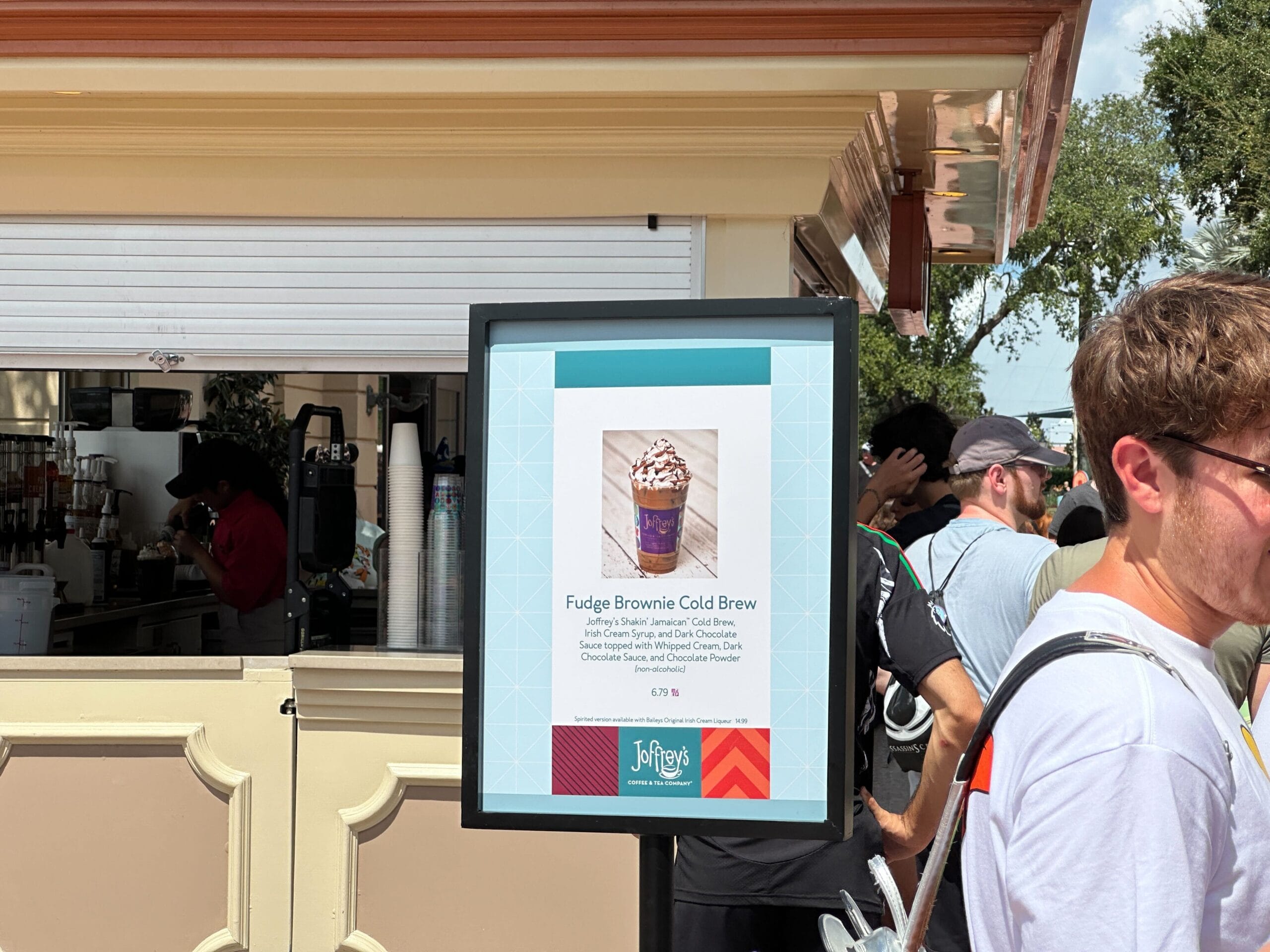 A sign displays a Fudge Brownie Cold Brew drink menu at the New Food & Wine coffee stand with people waiting in line.