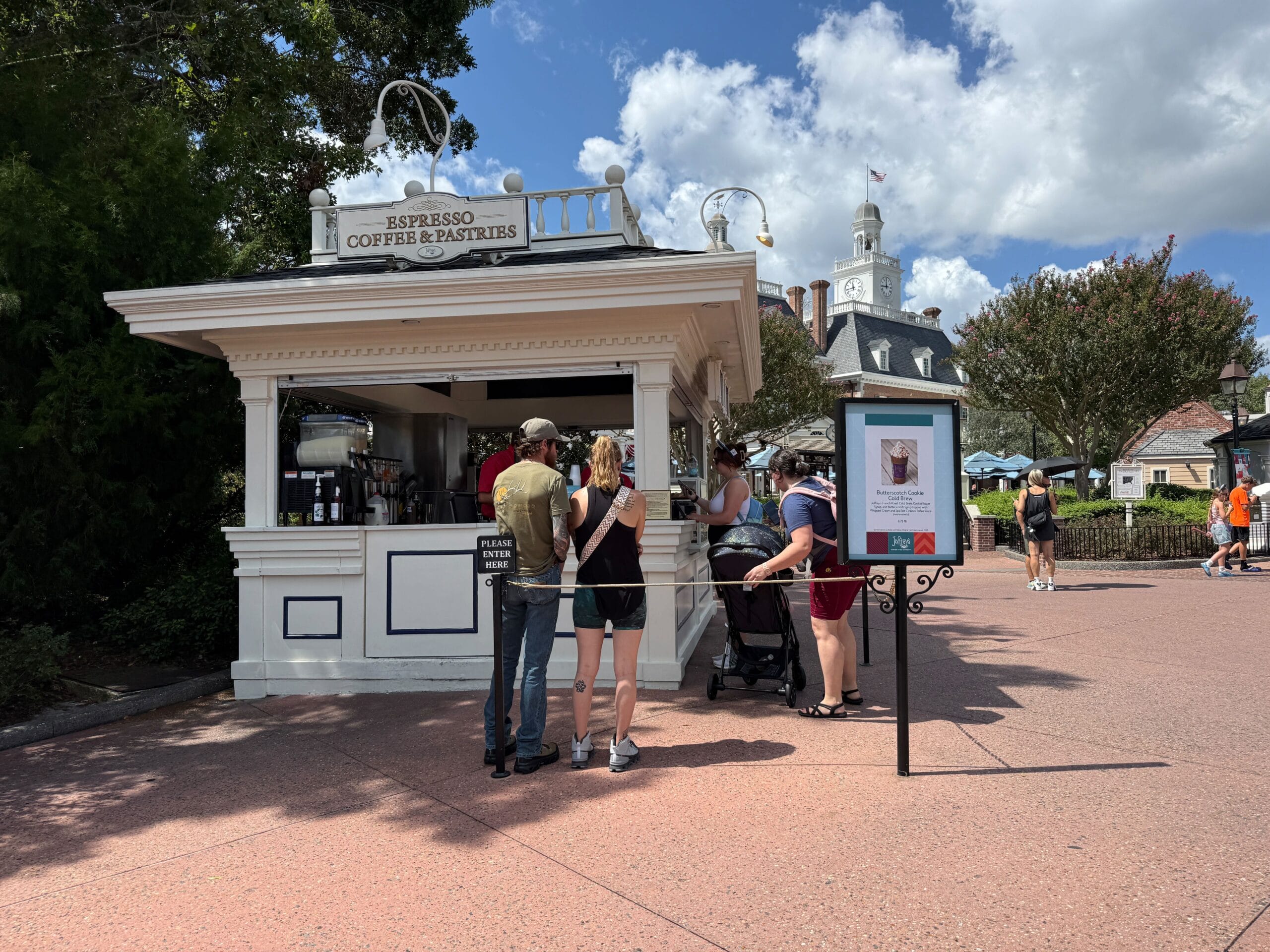 People stand in line at an outdoor Food & Wine kiosk for espresso and pastries on a sunny day with blue sky.