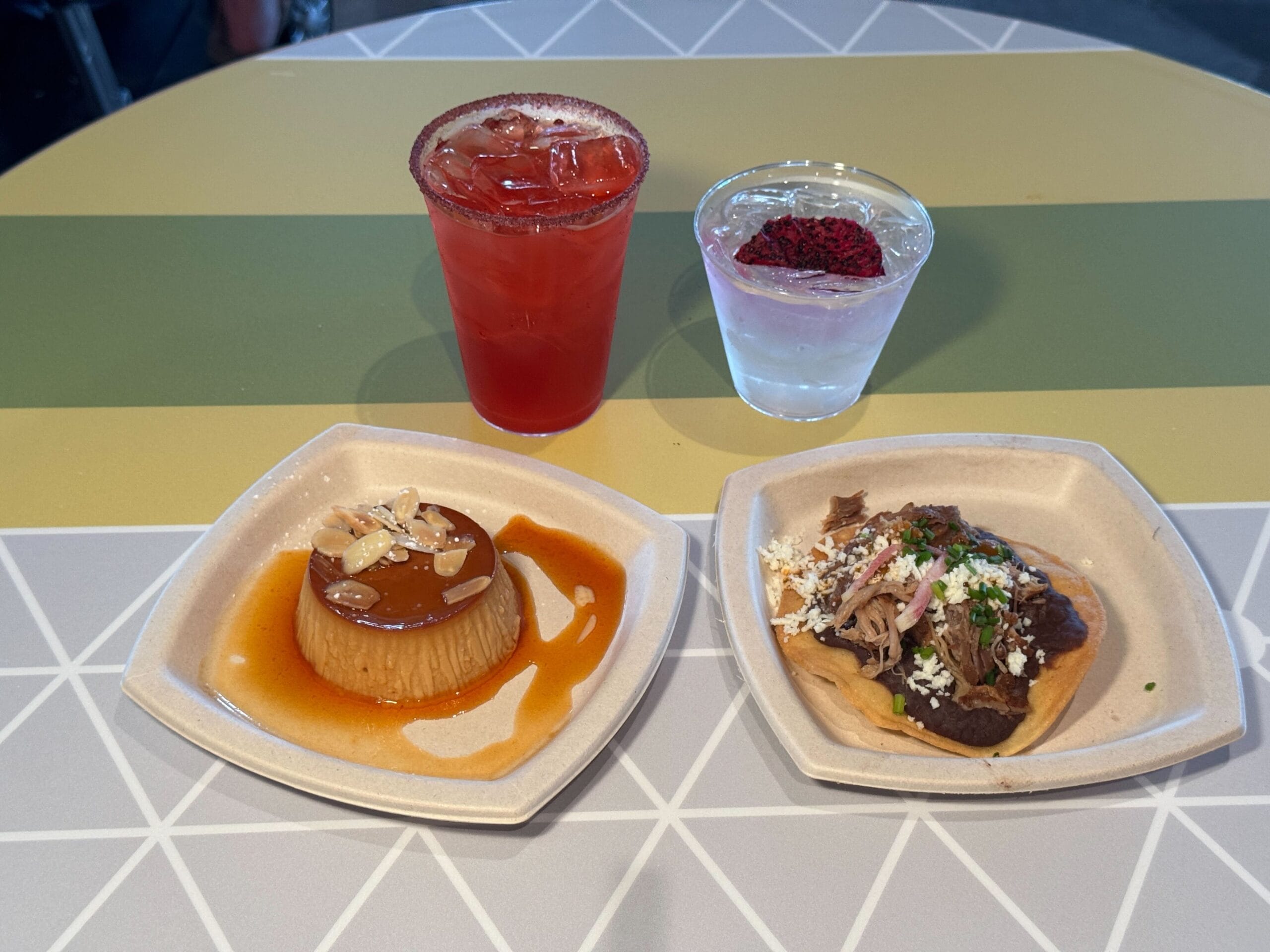 Two plates with flan and a taco, plus two drinks, at the 2025 EPCOT Food and Wine Festival on a geometric-patterned table.