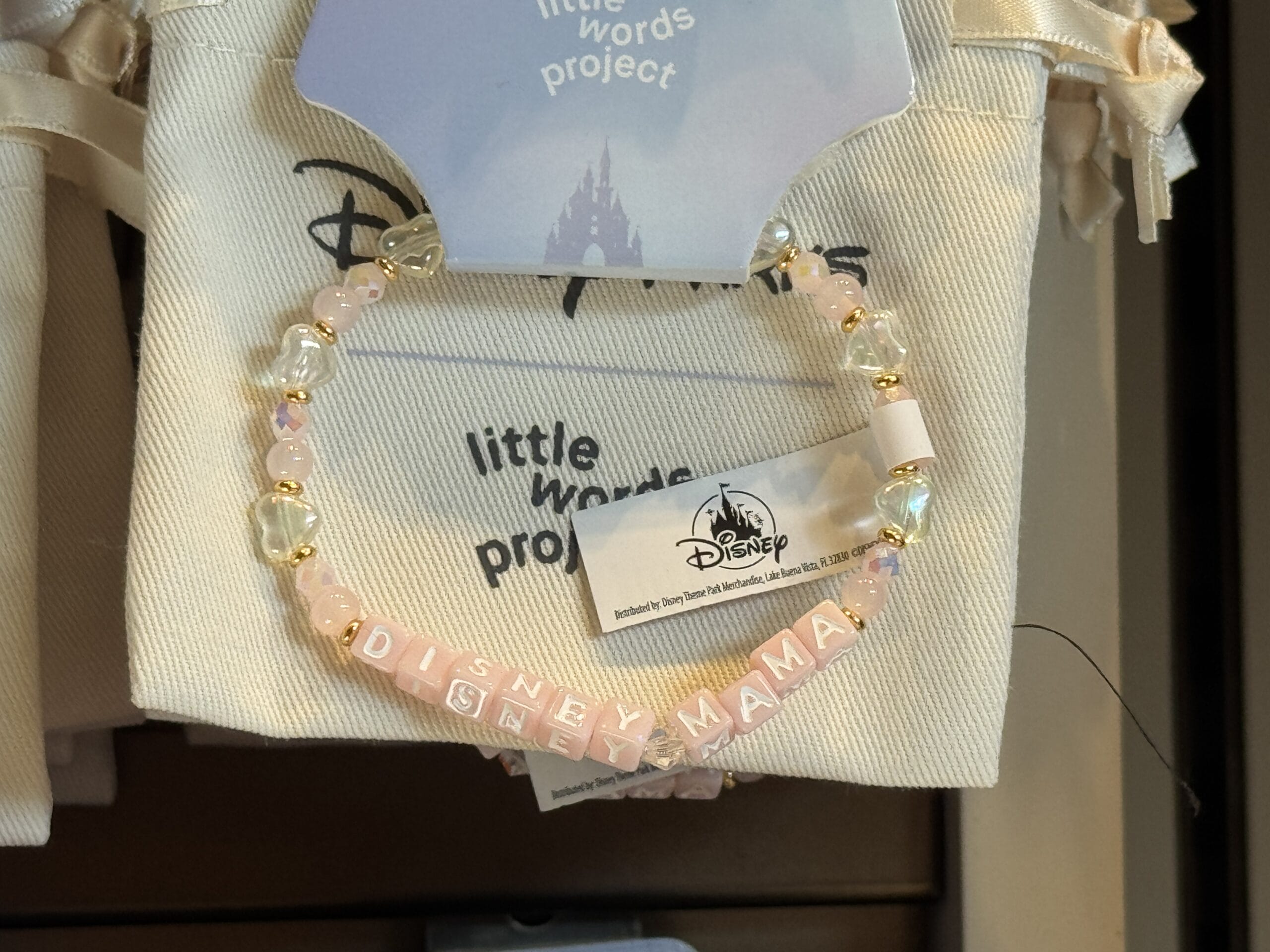 A beaded bracelet with pink and white letter beads spelling "DISNEY MAMA," spotted at Hollywood Studios.