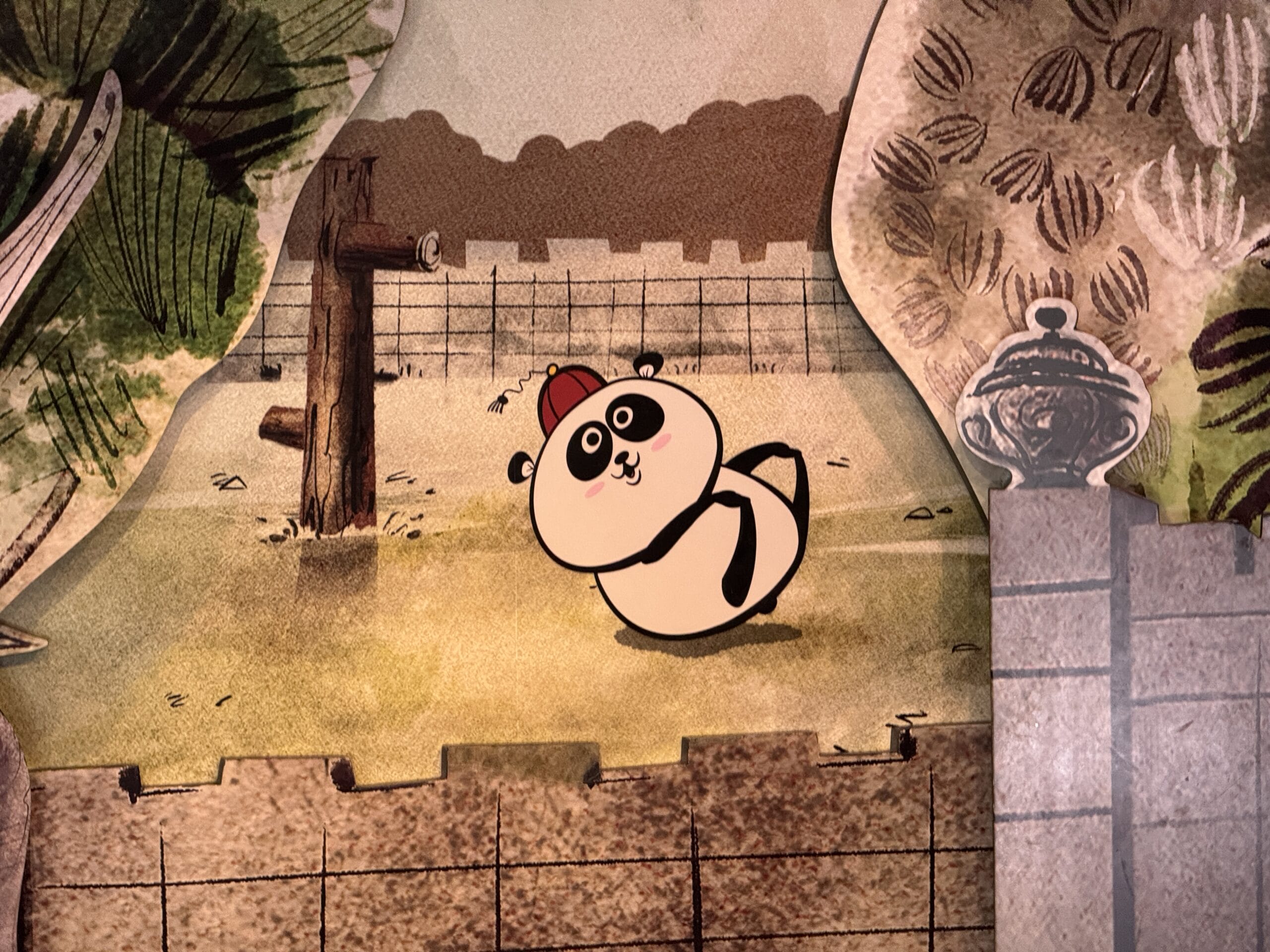 Illustrated panda in a red hat sits on grass behind a stone wall—perfect for a 2025 Hollywood Studios photo report.