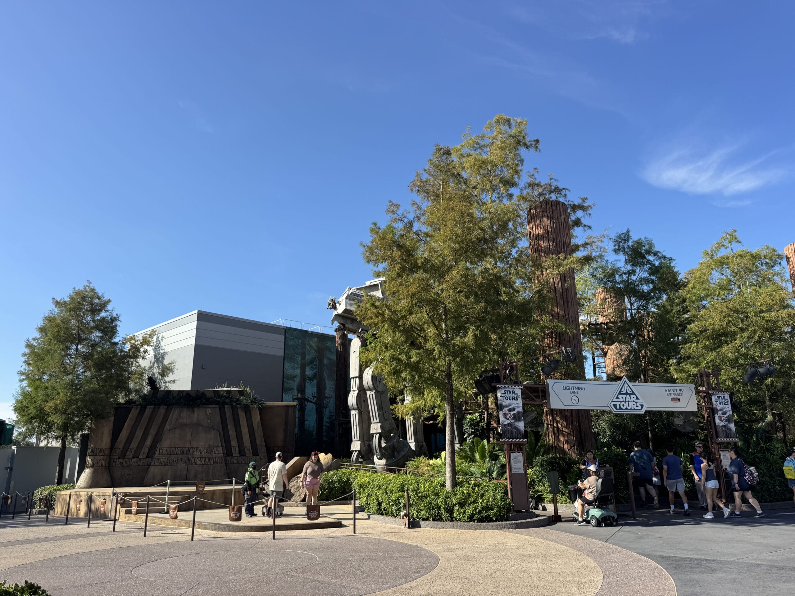 Entrance to Star Tours at Hollywood Studios, with trees, people, and blue skies. Nothing is Safe in Hollywood Studios!