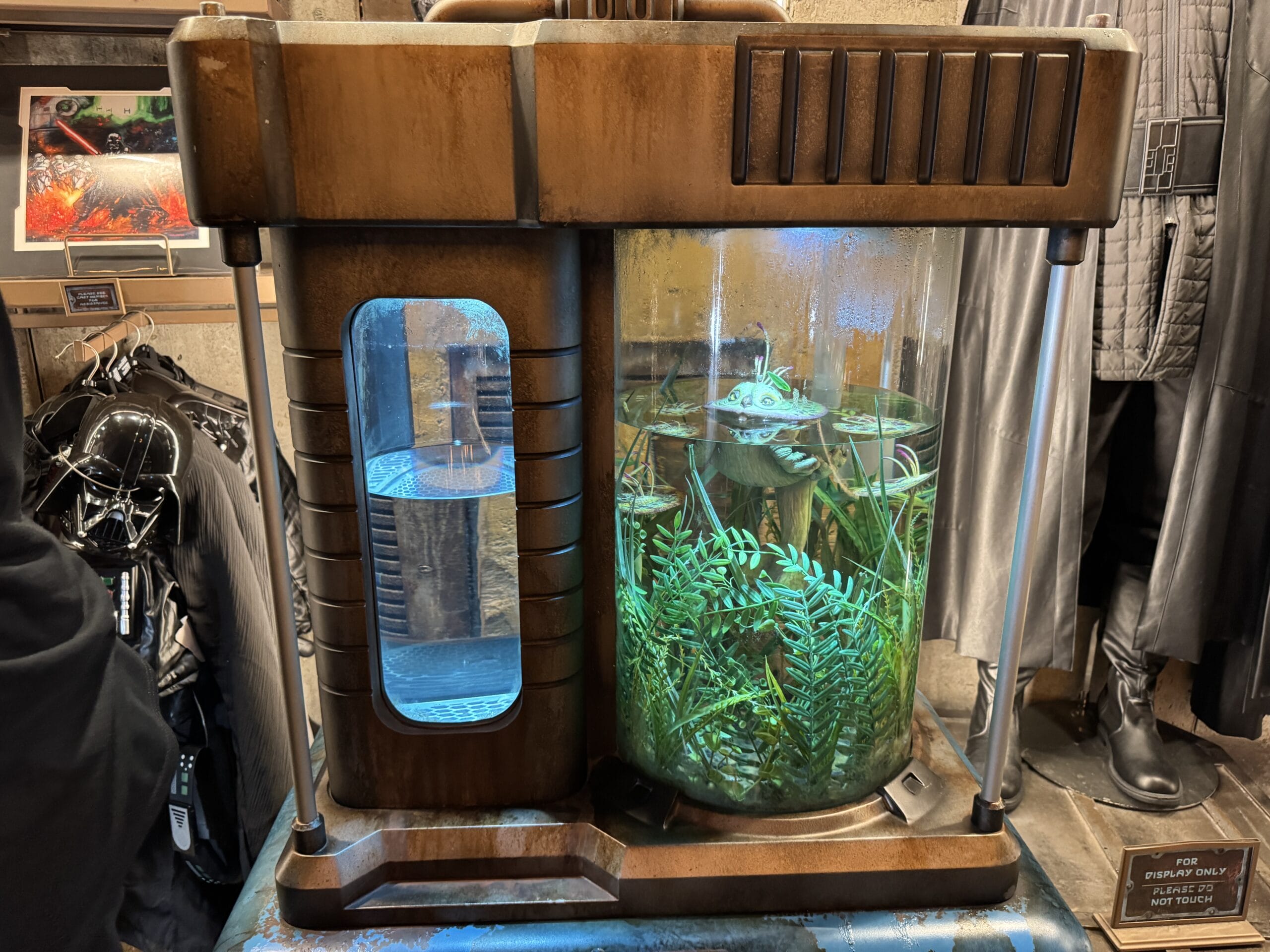 A sci-fi tank with glowing blue water and green plants, plus a floating droid, highlights the Hollywood Studios 2025 display.