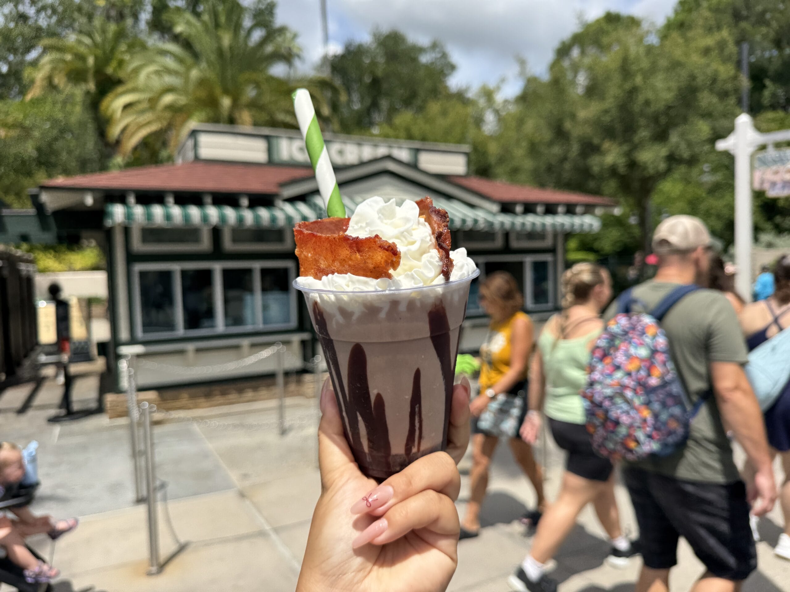 Hand holding a chocolate sundae with whipped cream and bacon outside an ice cream shop at Hollywood Studios.