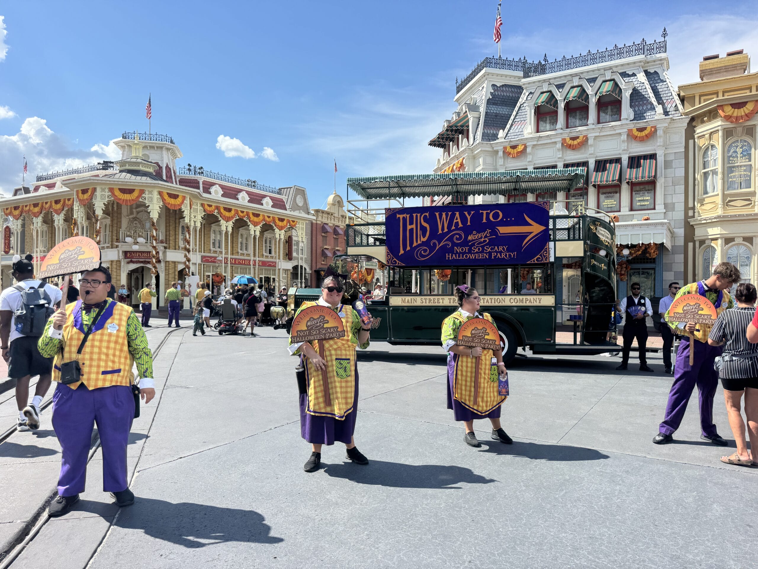 Four performers in Halloween costumes guide guests to an Oogie Boogie Bash on a sunny, festively decorated street.
