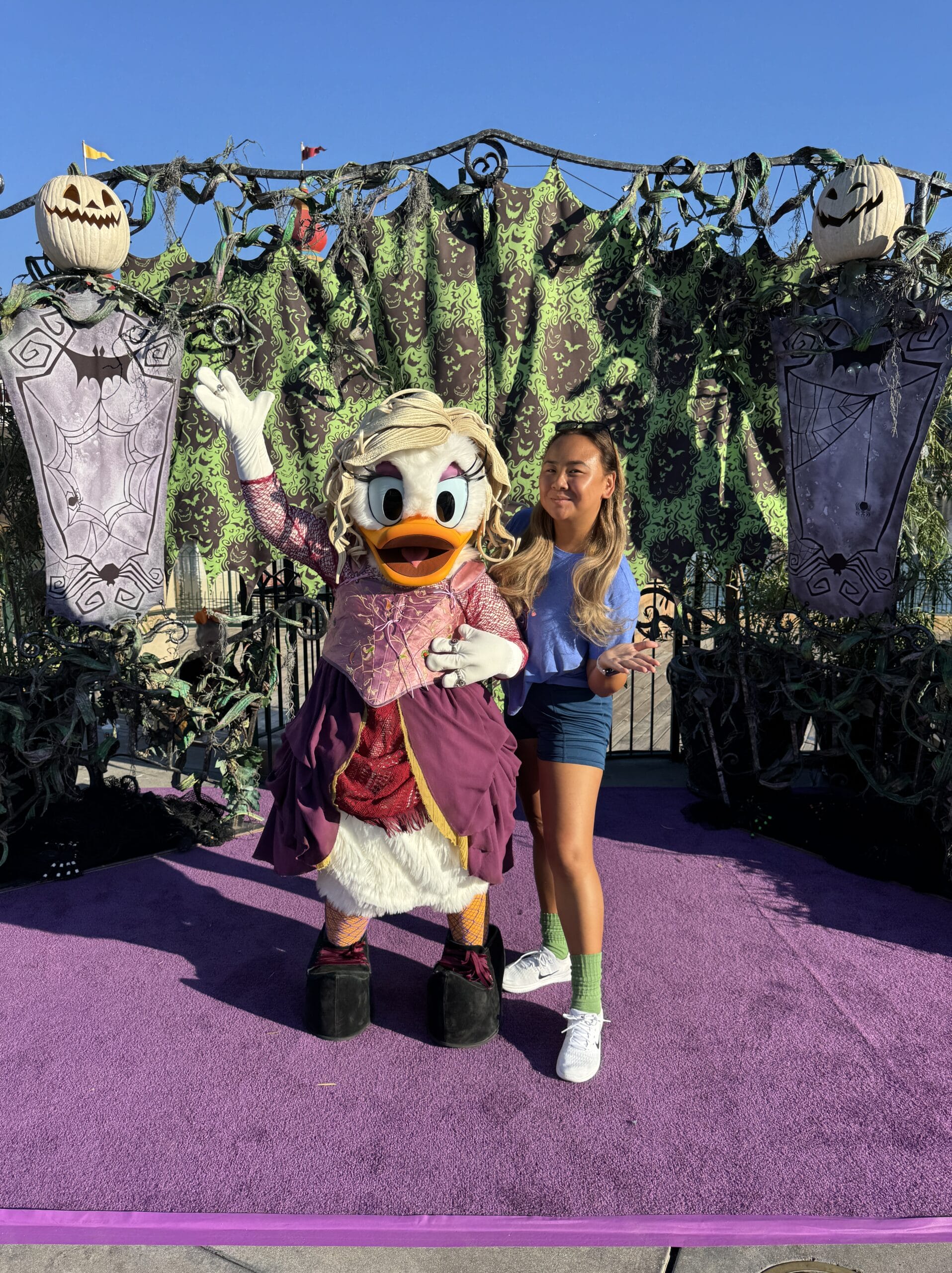 A woman poses with Daisy Duck in a Halloween costume at Mickey's Not So Scary Party, surrounded by spooky decorations.