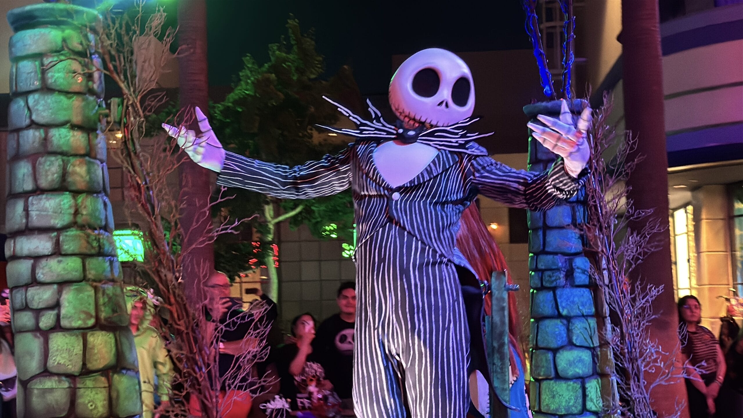 A person in a Jack Skellington costume poses at night between decorated pillars during Oogie Boogie Bash.