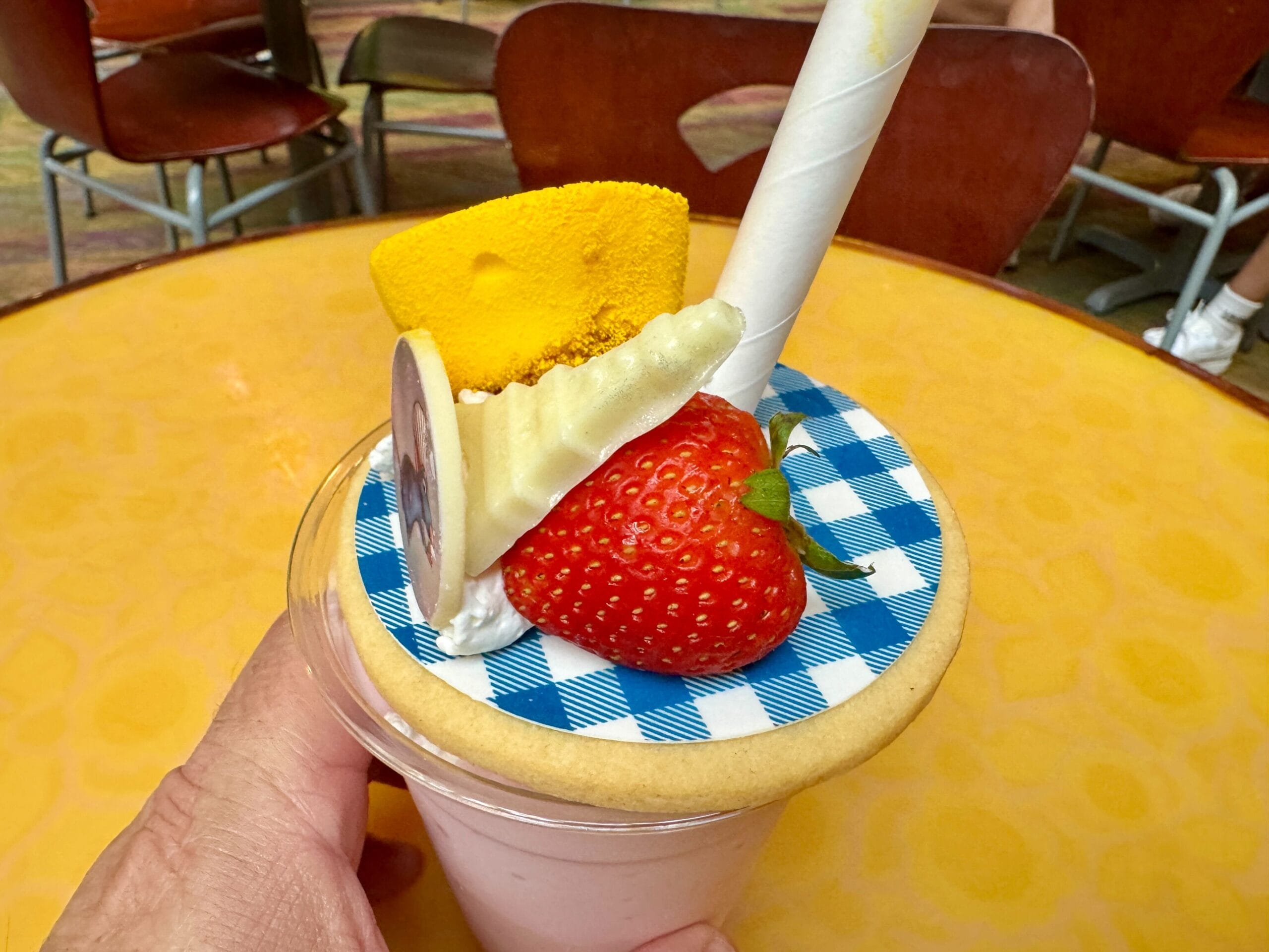 A hand holds a milkshake topped with a strawberry, yellow marshmallow, and blue checkered cookie lid at Food & Wine.