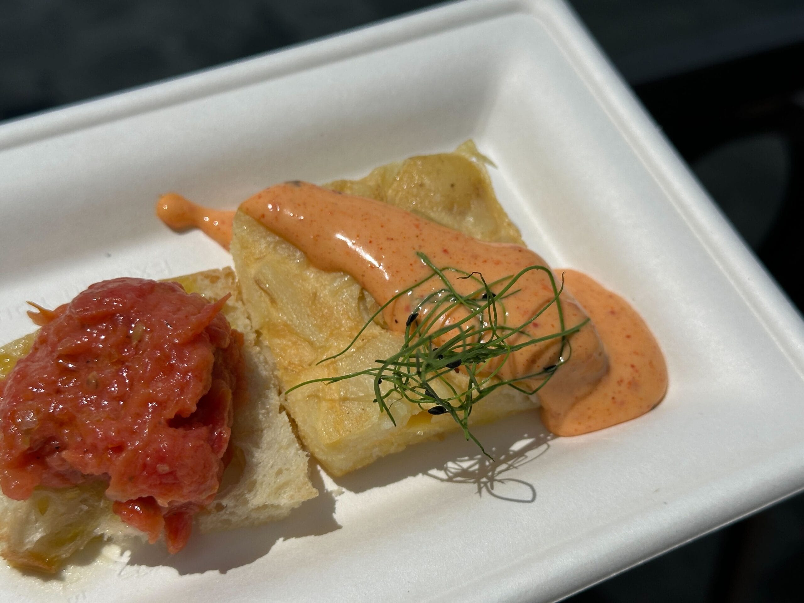 A slice of bread topped with tomato and sauce, garnished and served Food & Wine style on a white paper plate.