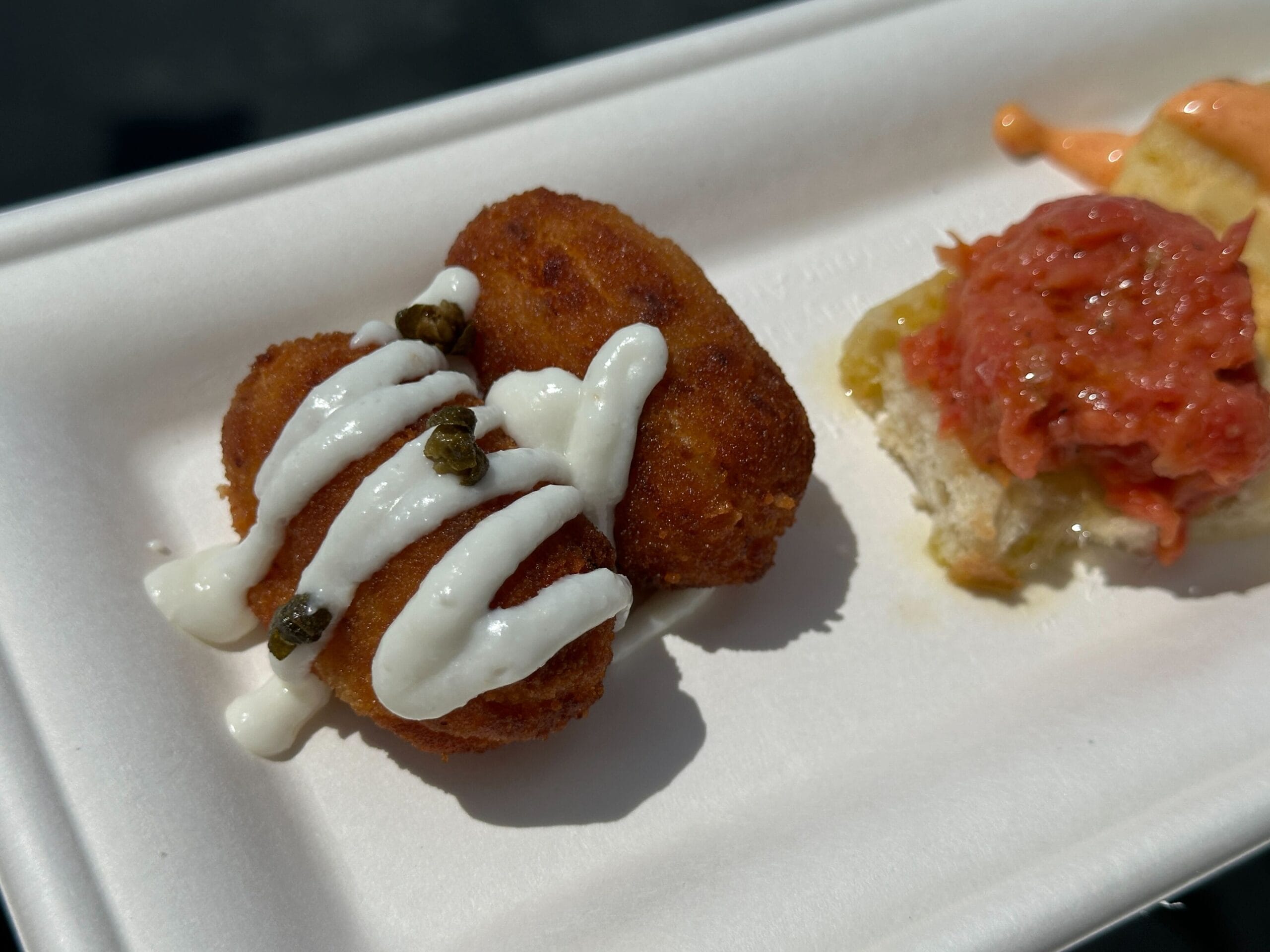 Two breaded fried croquettes topped with white sauce, served with a Food & Wine-inspired red-spread bread.