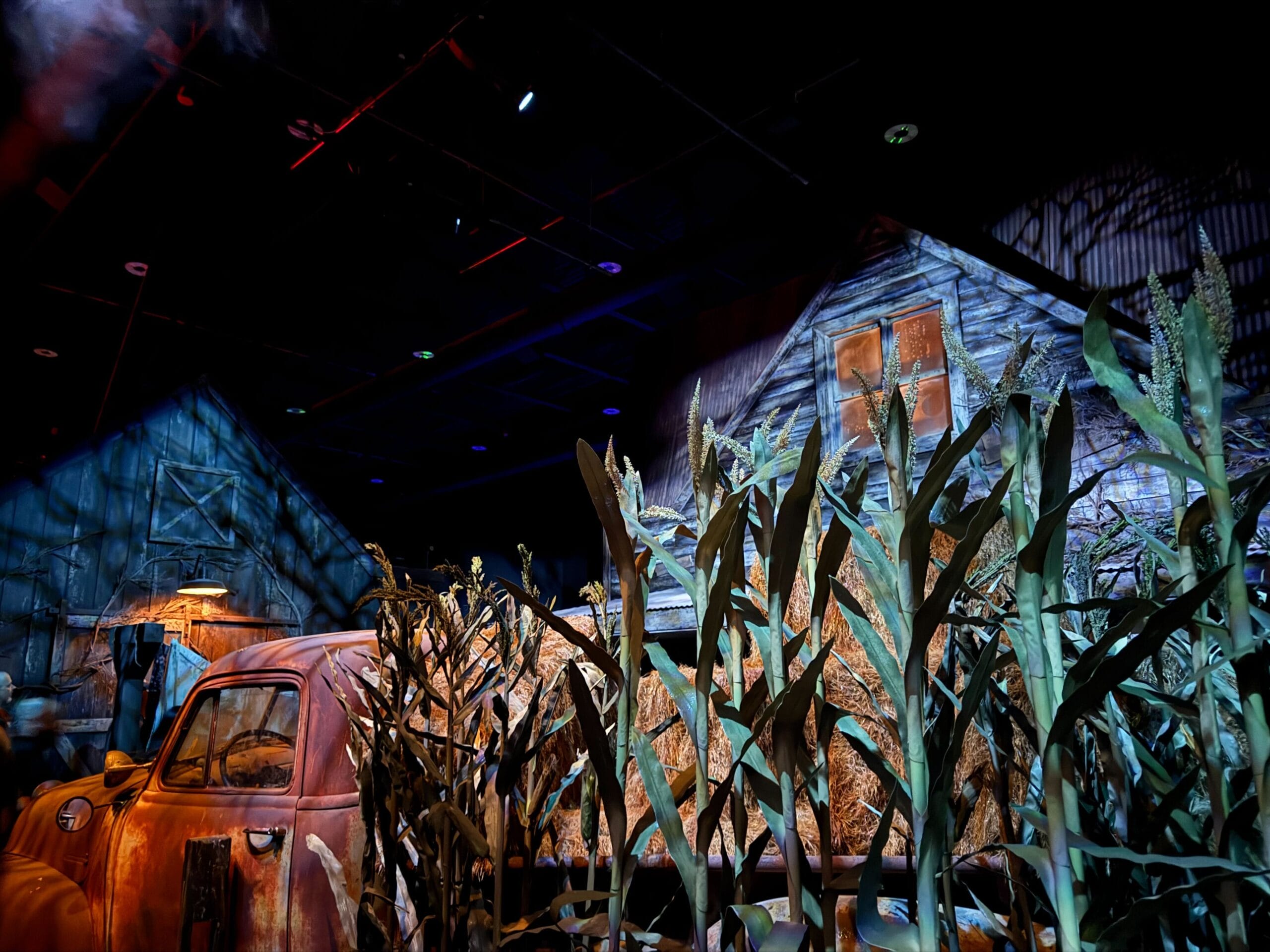 A rusty old truck sits amid tall cornstalks by two barns, part of the Scarecrow: The Reaping House full tour.