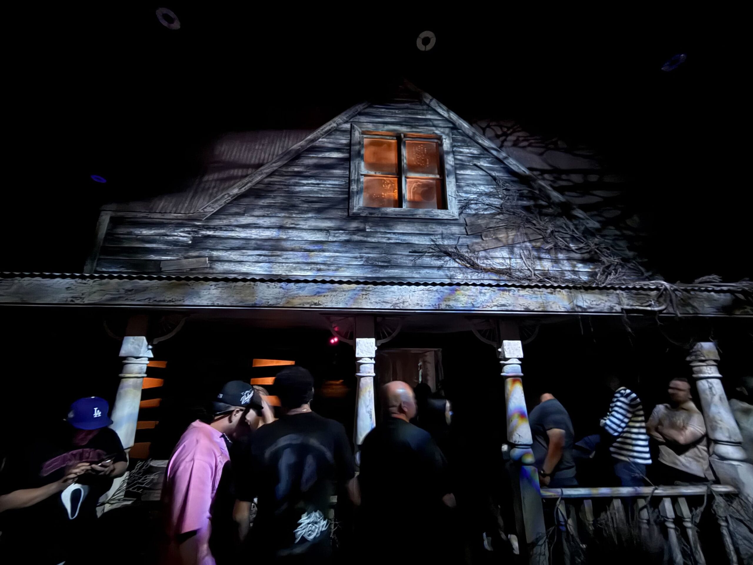 A group tours Scarecrow: The Reaping House, standing before its spooky, dimly lit façade at night.