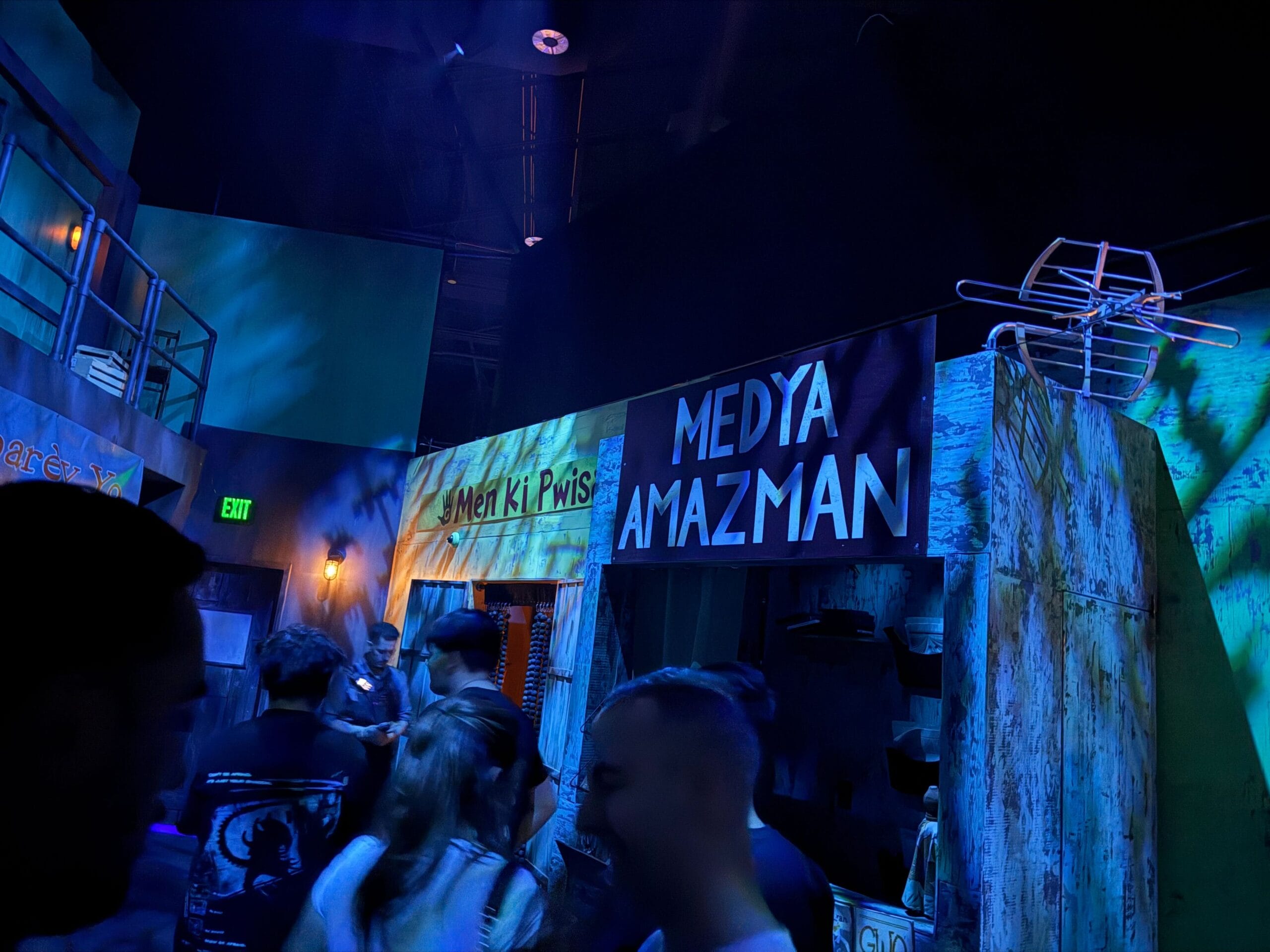 People stand in a dimly lit, blue-toned room with signs, exploring the Exorcist The Believer House full tour.