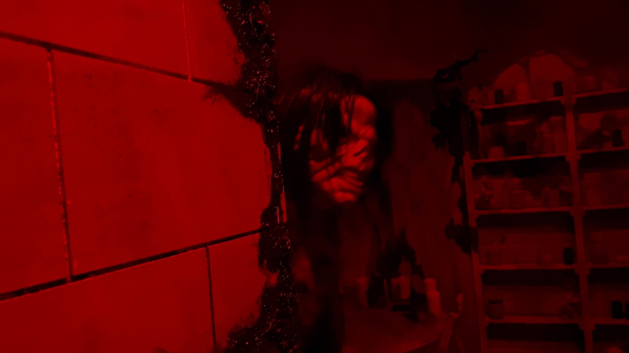A distorted, ghostly face emerges from a cracked, red-lit bathroom wall—like a scene from Exorcist: Believer.