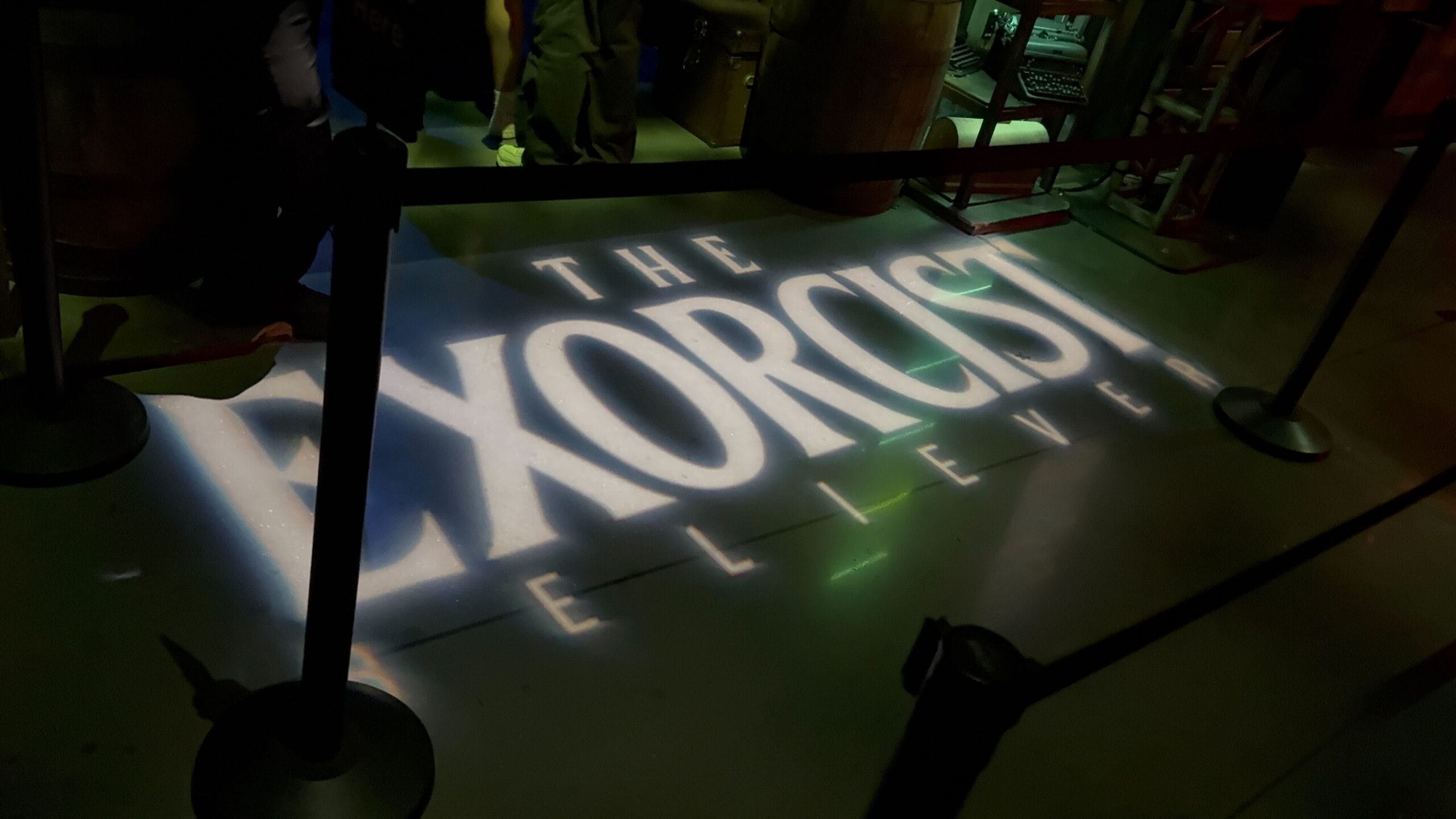 The Exorcist: Believer House logo is projected onto the floor at Universal Horror Unleashed, partially blocked by stanchions.