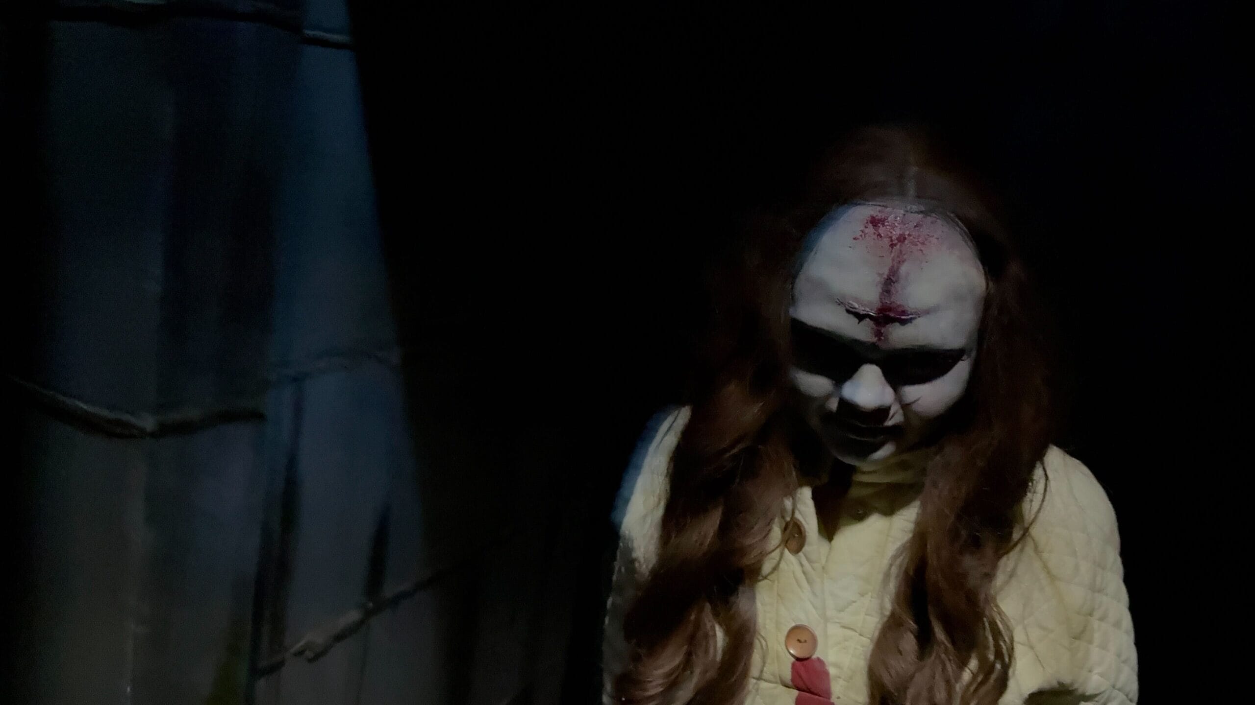 A creepy doll-like figure with long hair and a bloodied forehead haunts this Universal Horror Unleashed-inspired house tour.